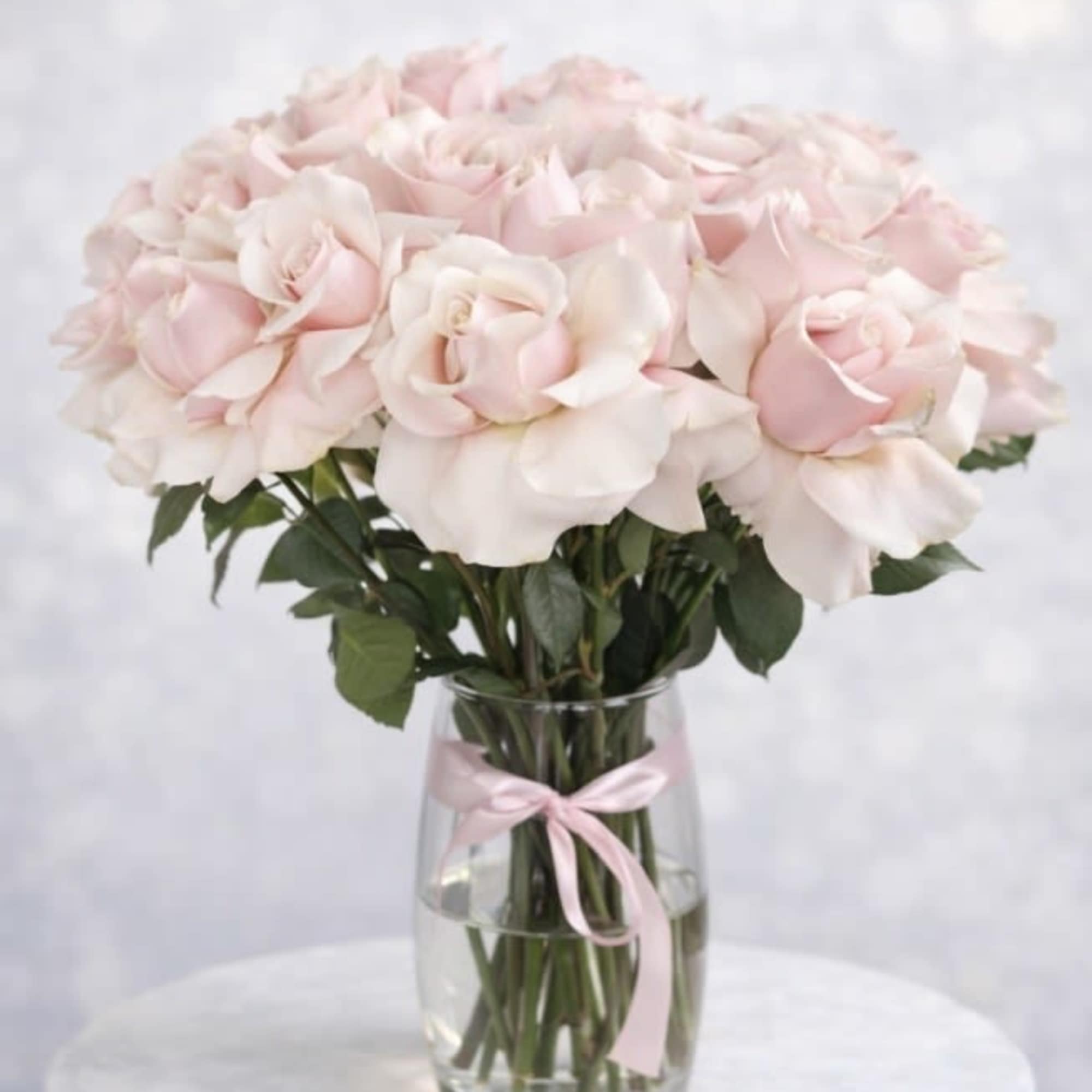 Pale pink roses arranged in a clear glass vase with a pink ribbon