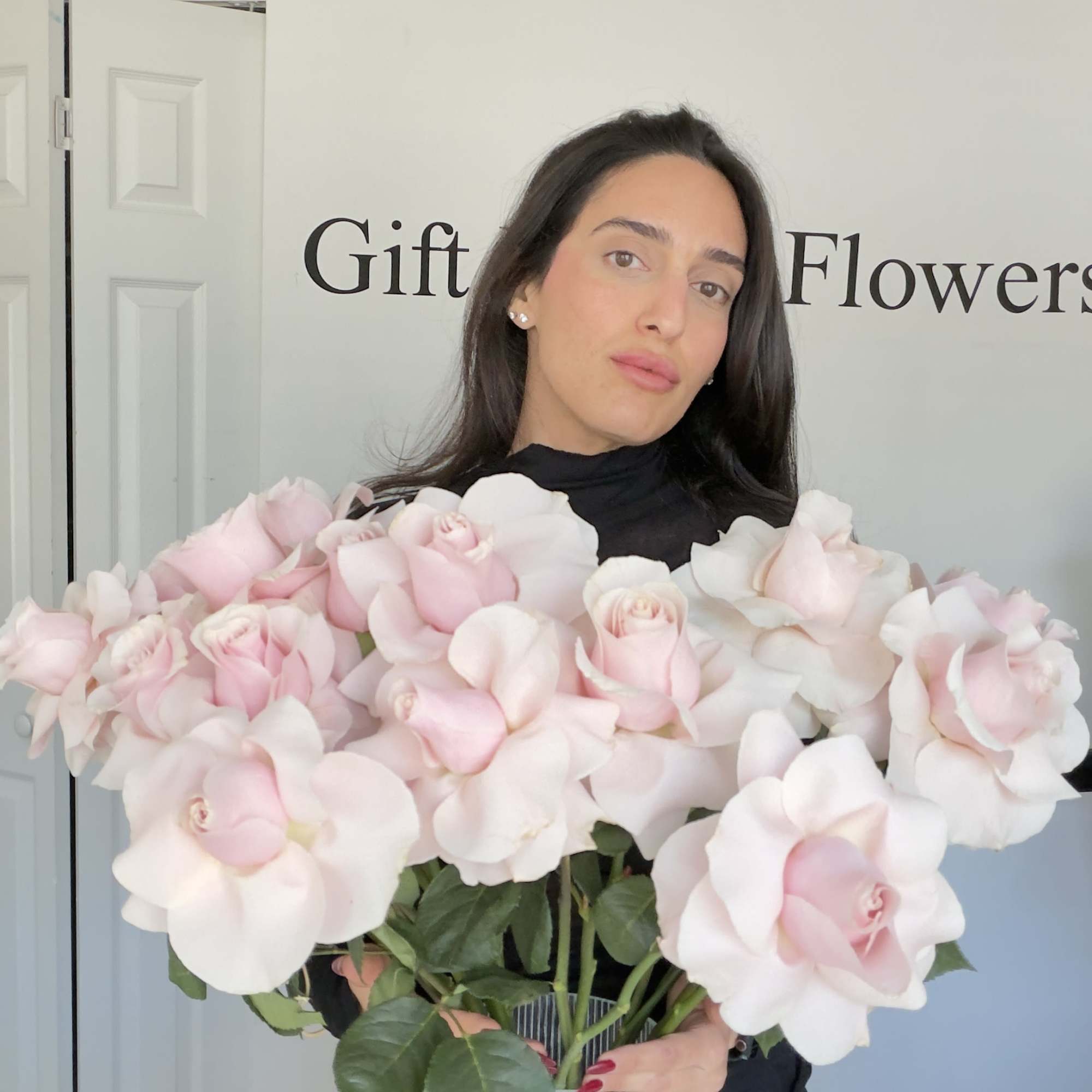 Woman holding a large bouquet of pale pink and white roses in a clear vase