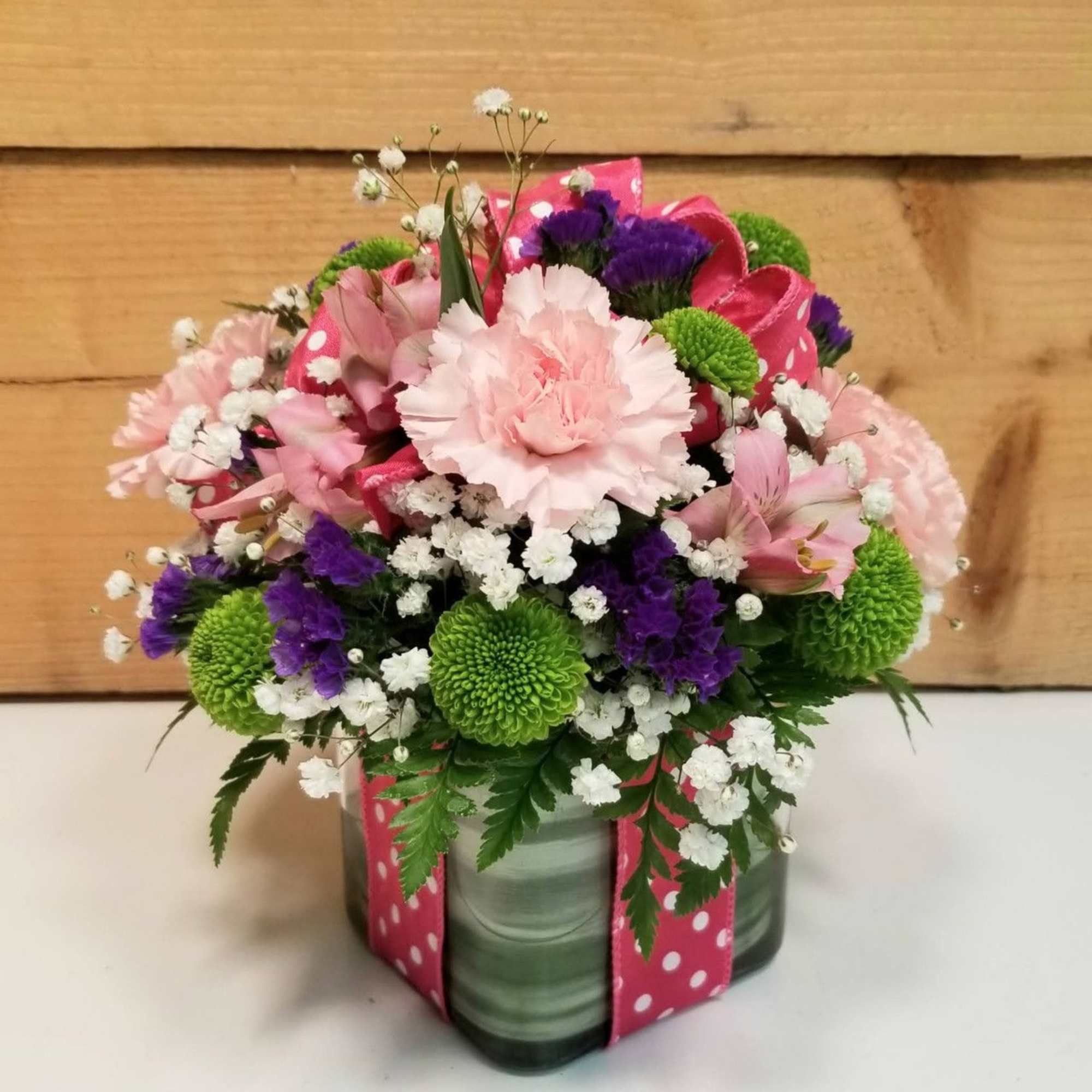 Pink and purple mixed bouquet in a square glass vase with a polka-dot ribbon