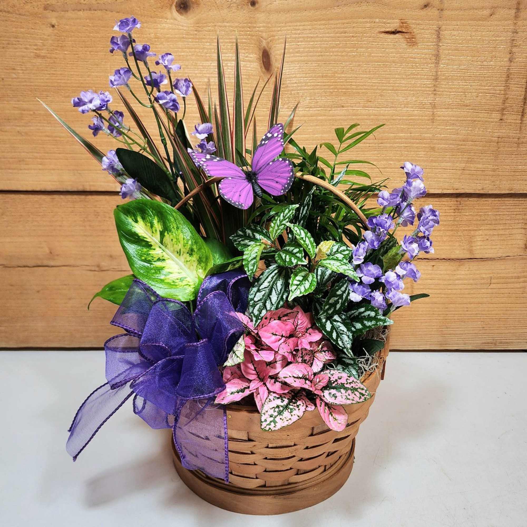 Potted plant arrangement with purple flowers and a purple ribbon in a basket