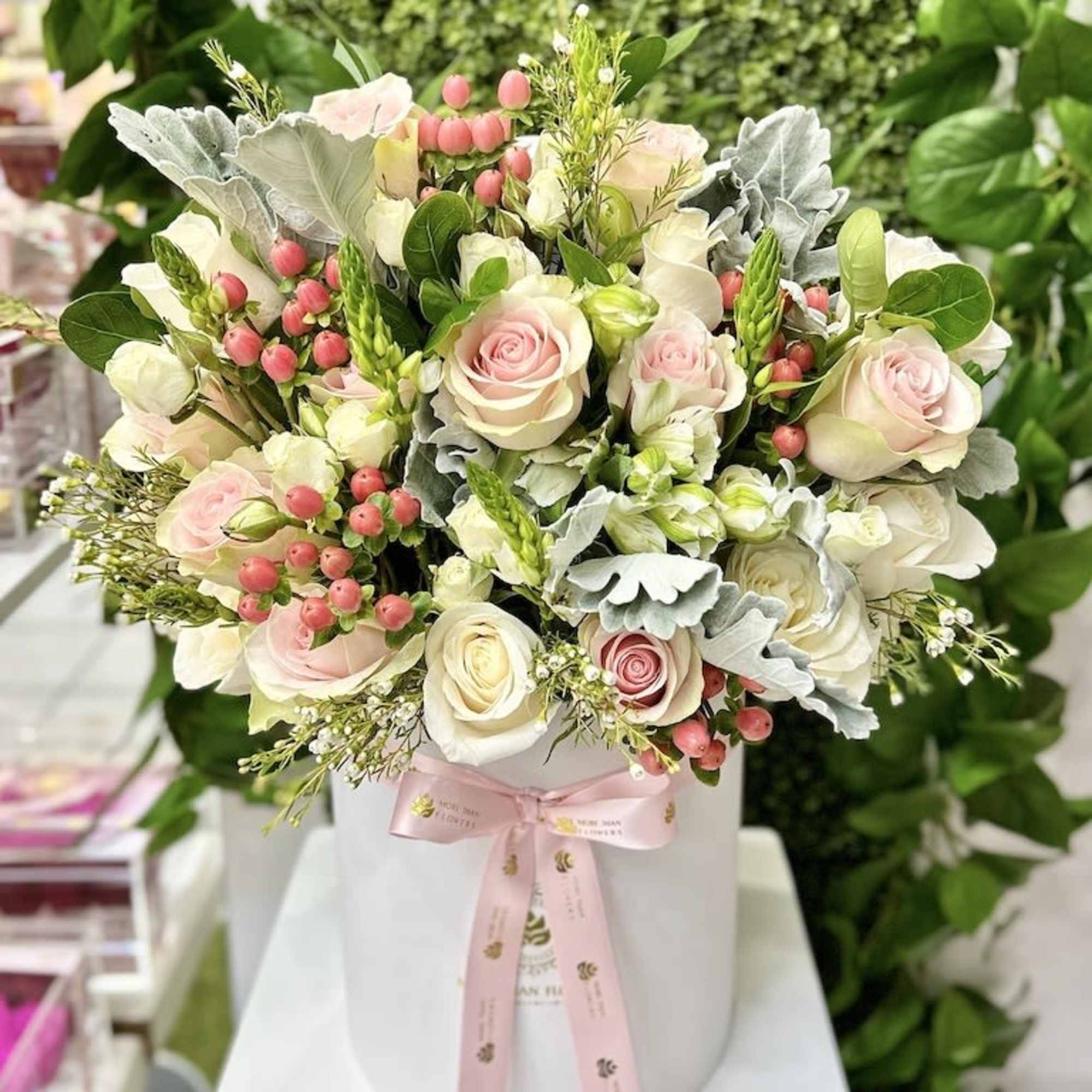 Blush and white rose arrangement with pink berries in a white hatbox tied with a pink ribbon