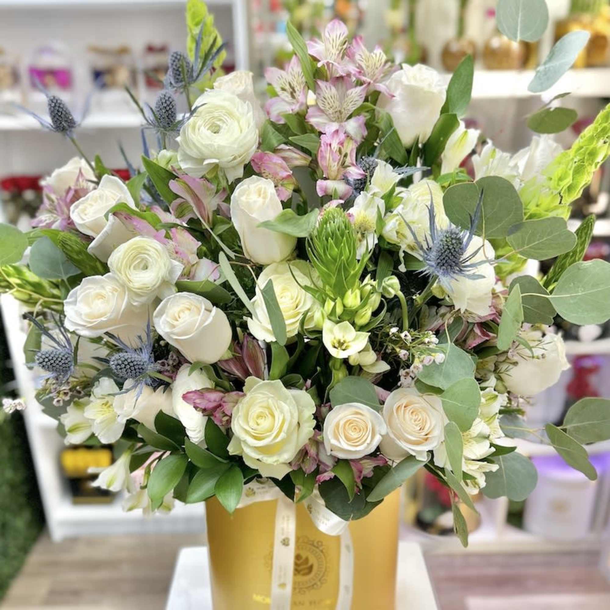 Tall arrangement of white roses and mixed flowers in a gold hatbox container