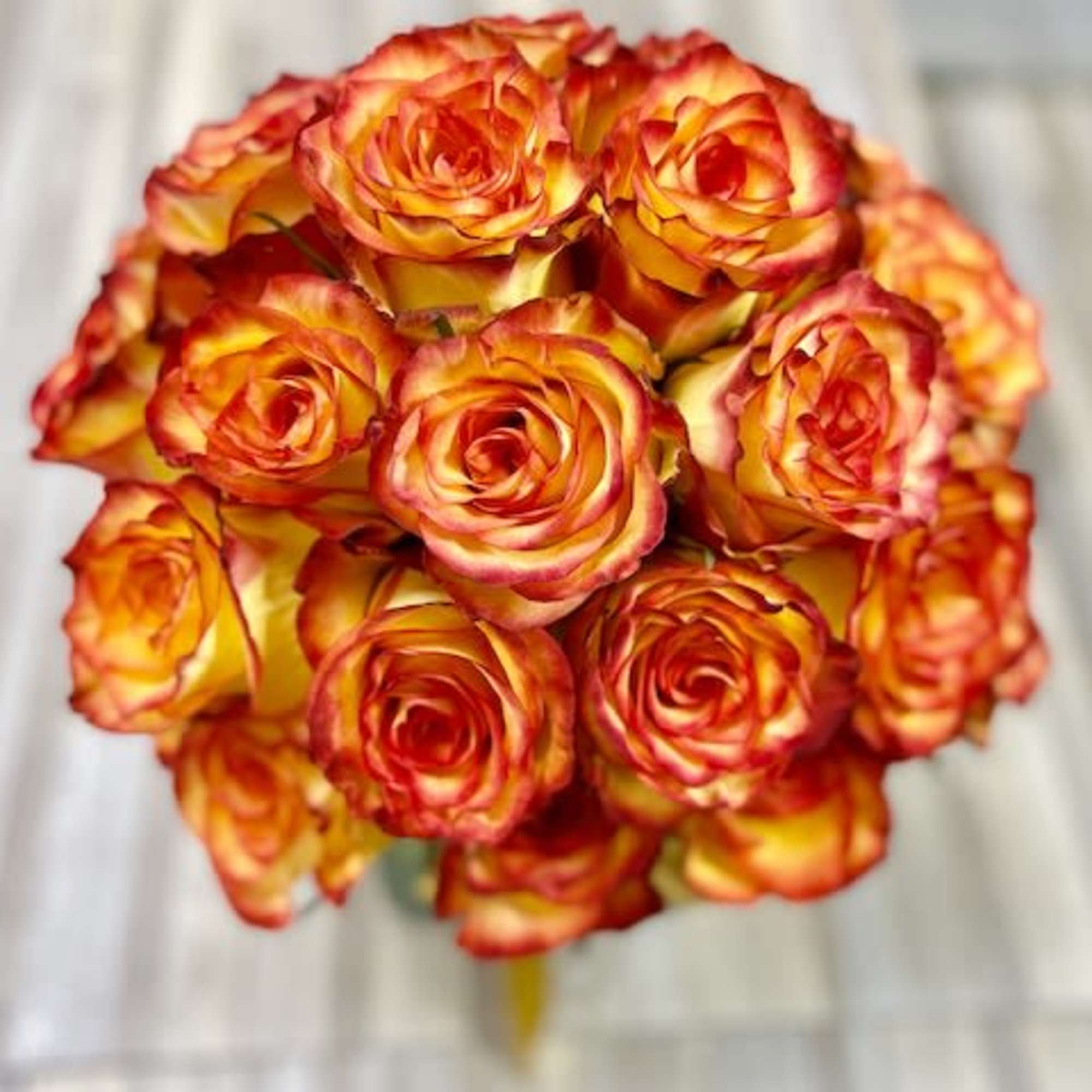 Round bouquet of orange and yellow bi-color roses with red edges on a light wood surface