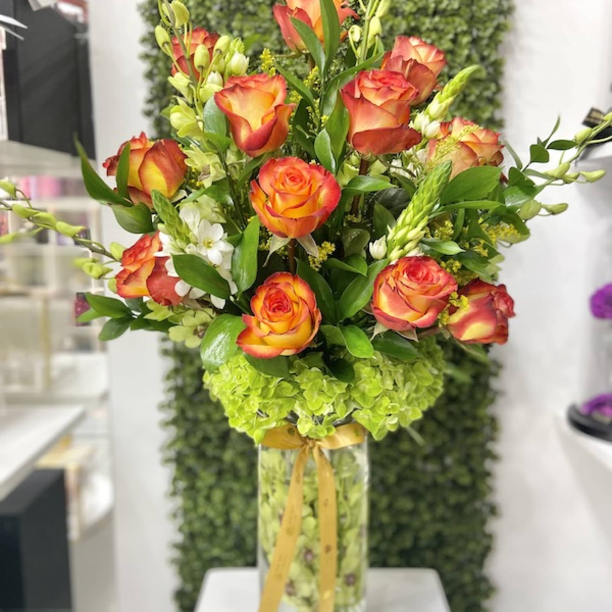 Tall arrangement of orange roses and green hydrangeas in a clear glass vase with ribbon