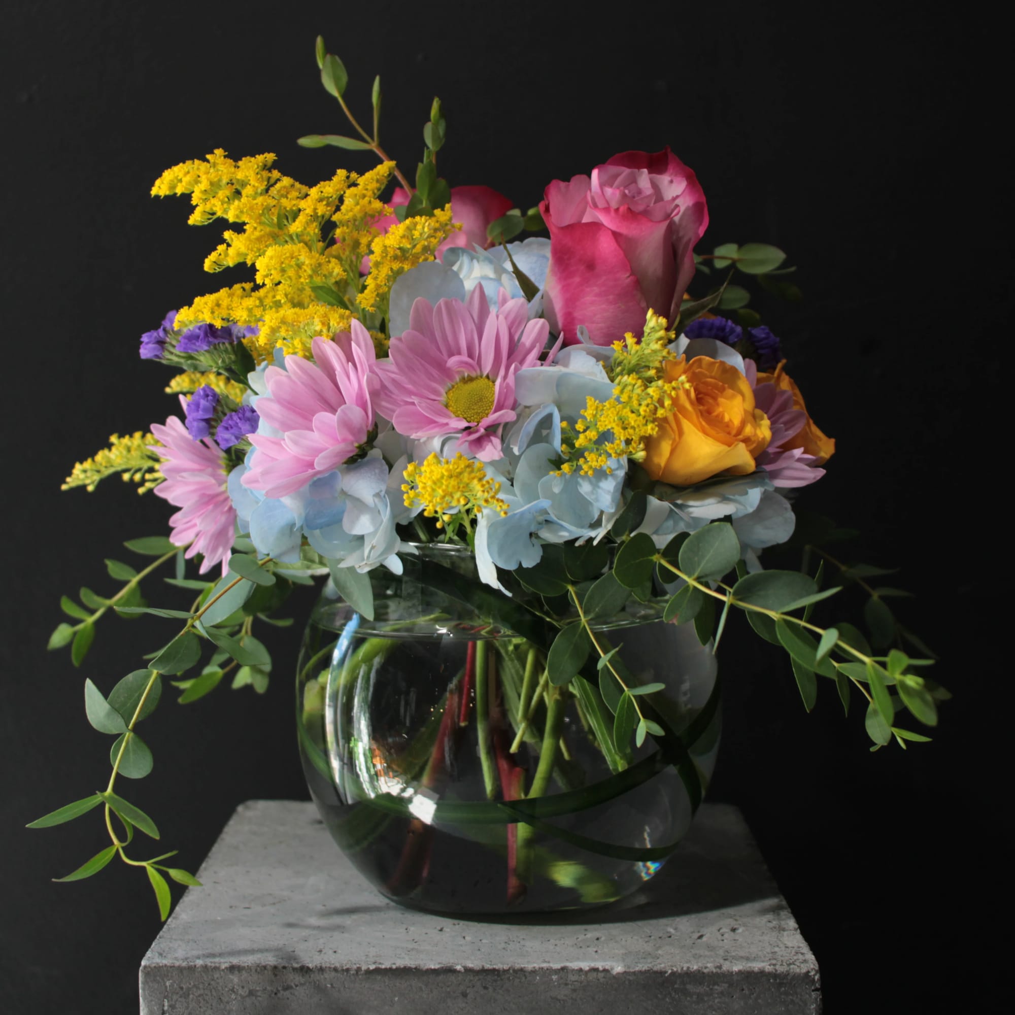 Mixed bouquet of pink roses, daisies, and yellow flowers in a glass vase