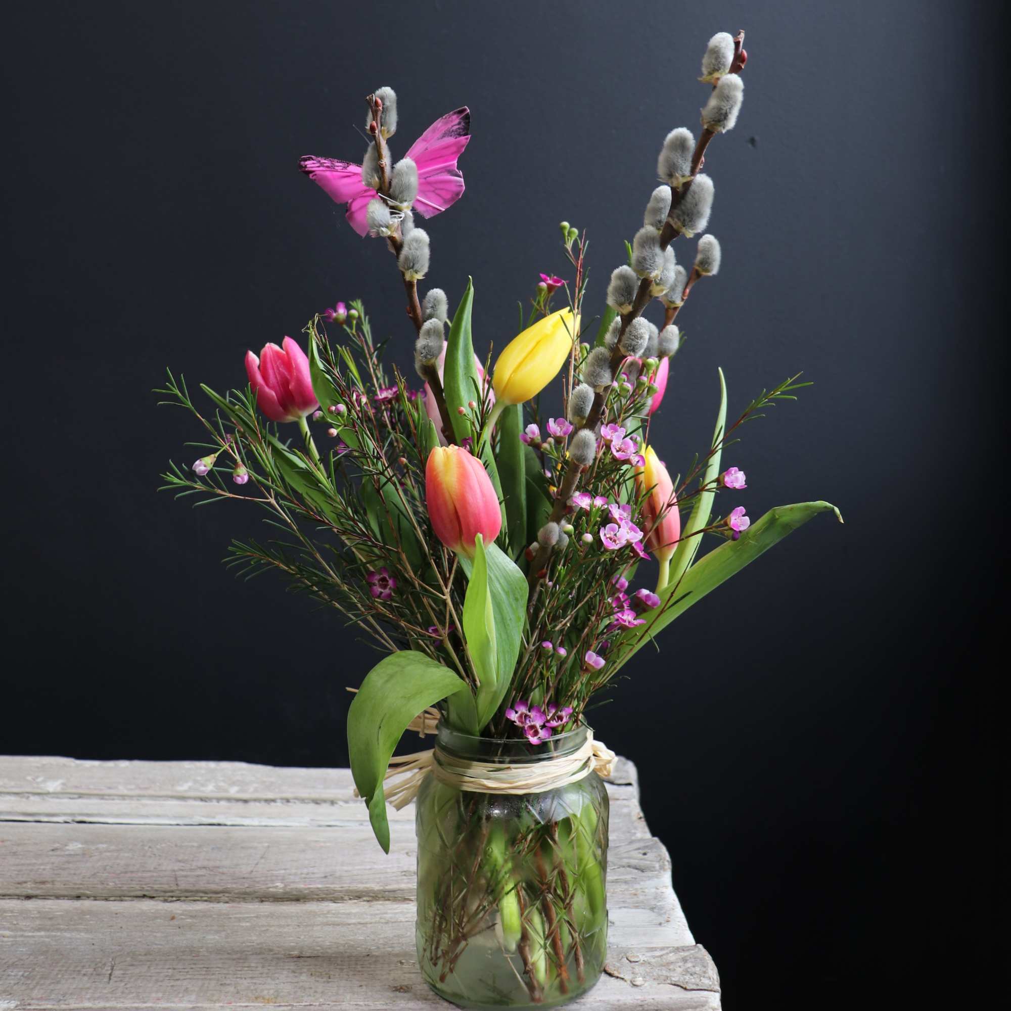 Tulips and pussy willow in a glass jar with a butterfly decoration