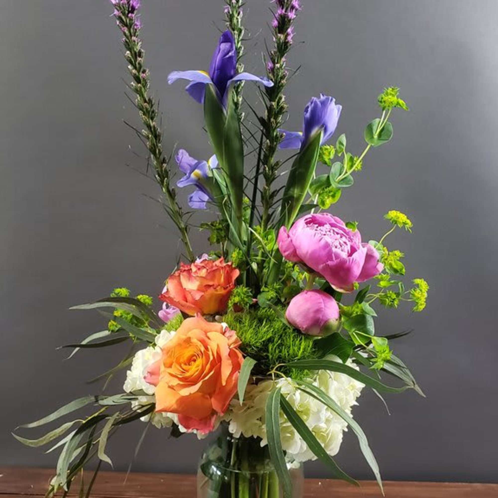 Tall mixed bouquet in a glass vase with purple spikes and pink, orange, and white blooms