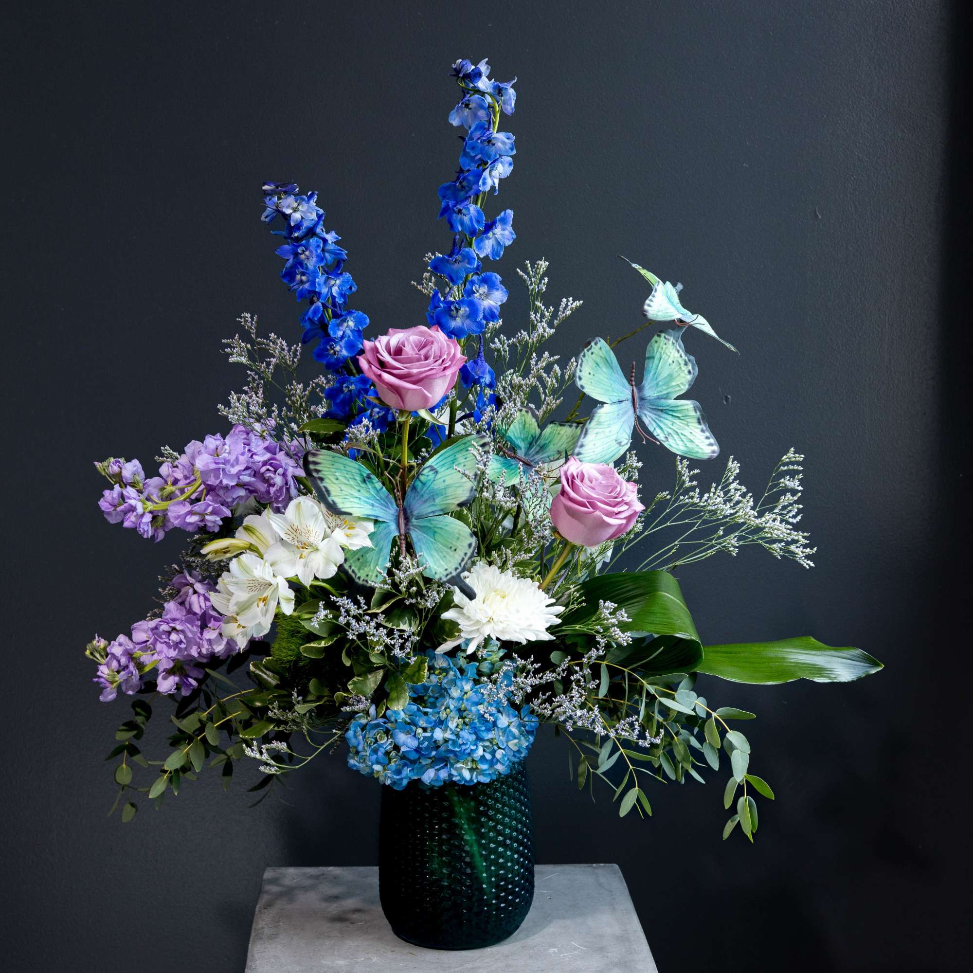 Tall floral arrangement with blue, purple, and white flowers in a dark vase