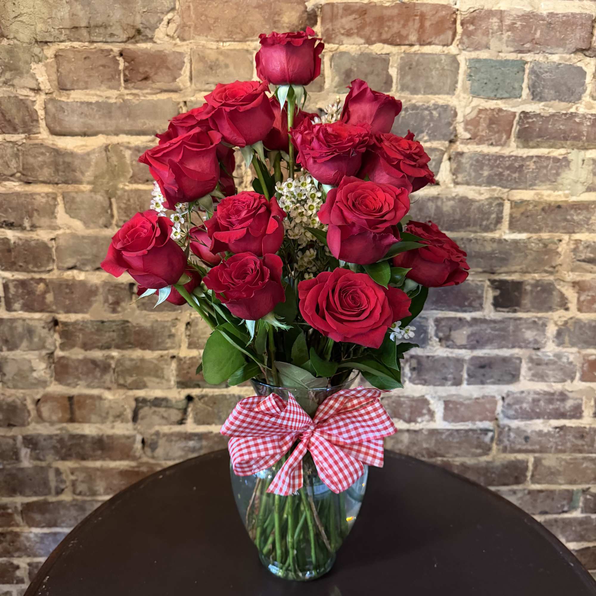 Red roses arranged in a clear glass vase with a gingham bow