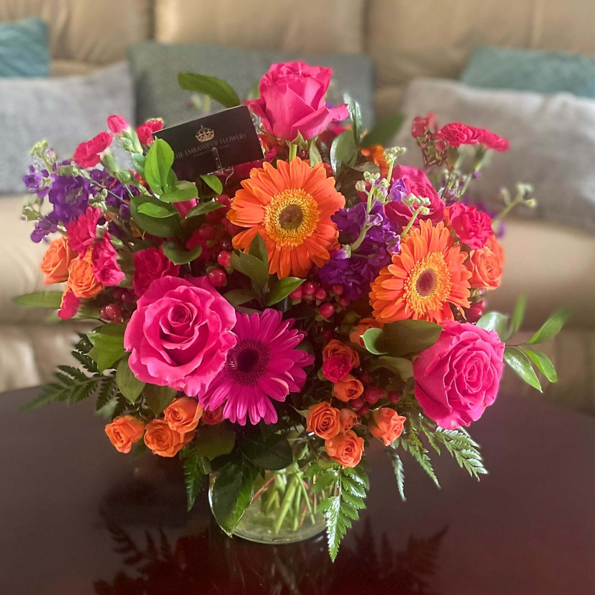 Bright mixed bouquet of pink roses, orange gerberas, and purple flowers in a glass vase