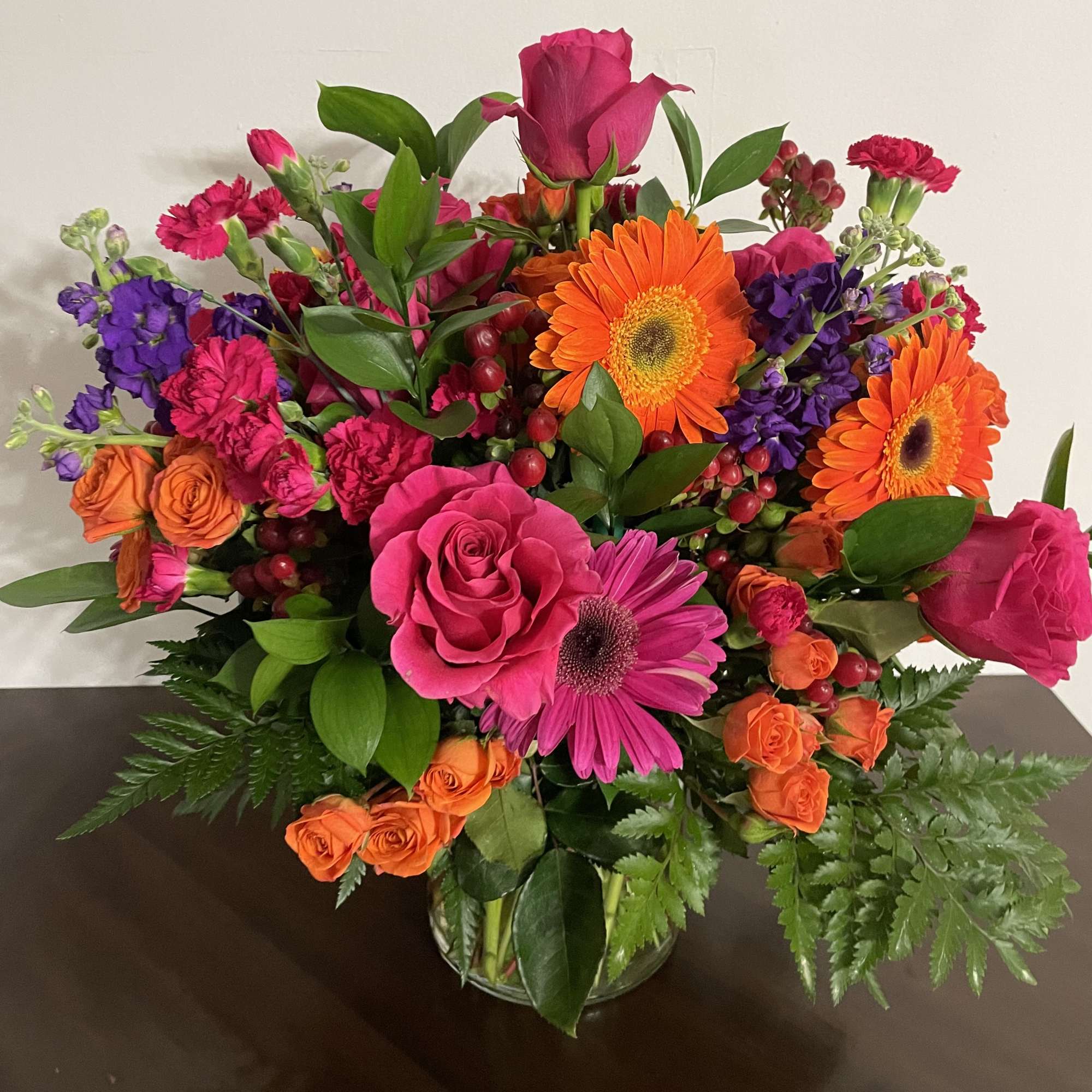 Bright mixed bouquet with pink roses, orange gerberas, and purple flowers in a glass vase