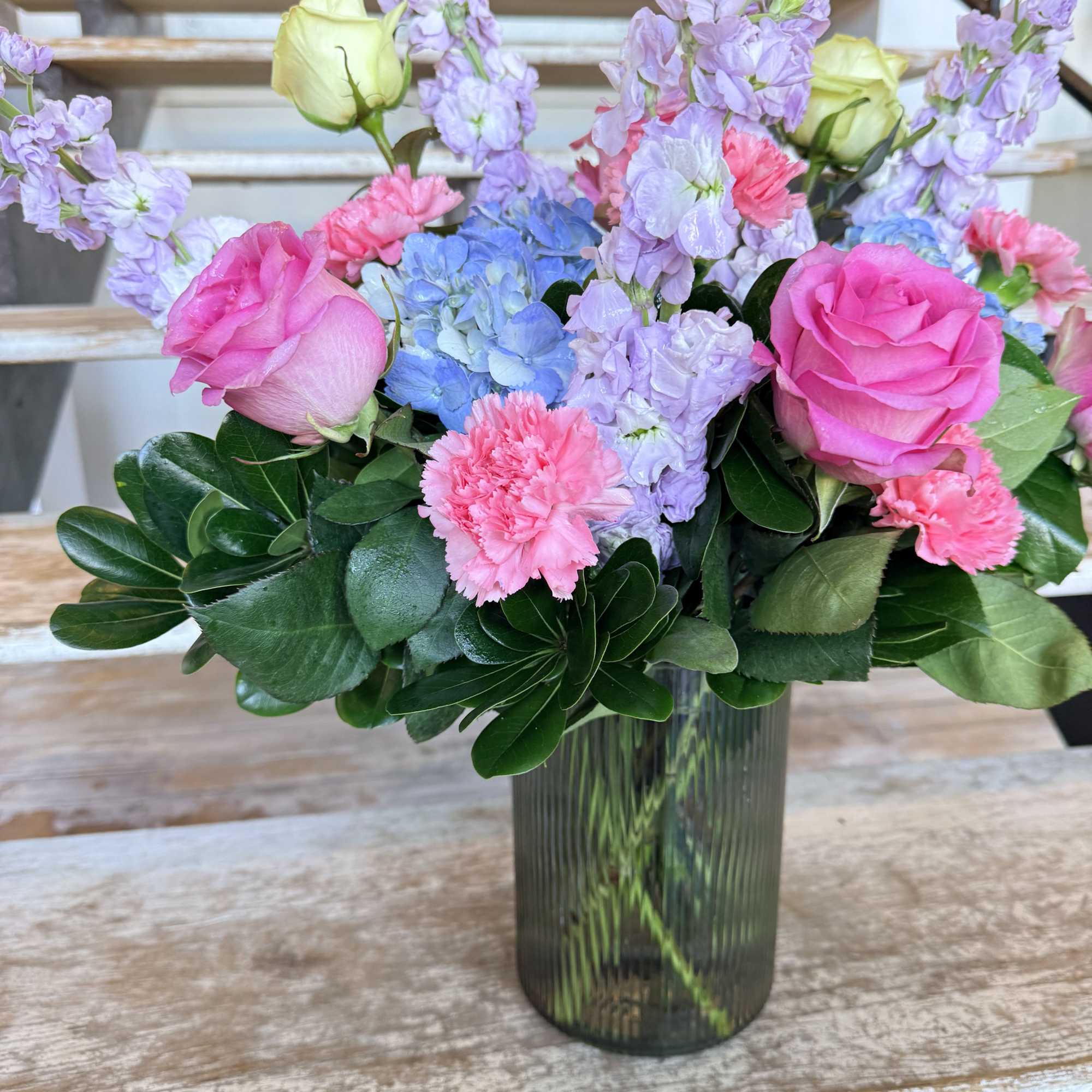 Pink roses, blue hydrangeas, and lavender stock in a glass vase