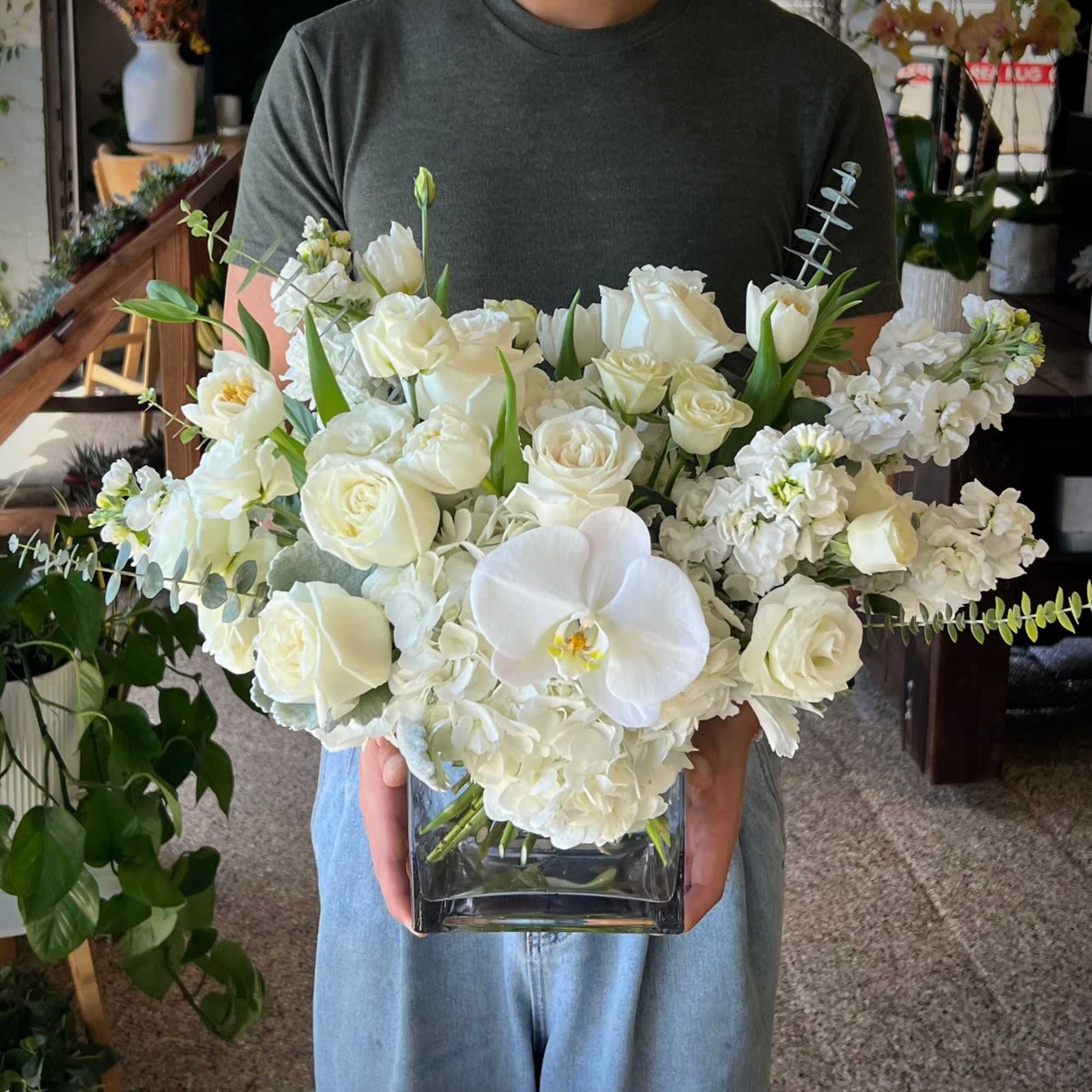 White floral arrangement in a square glass vase with roses and orchids