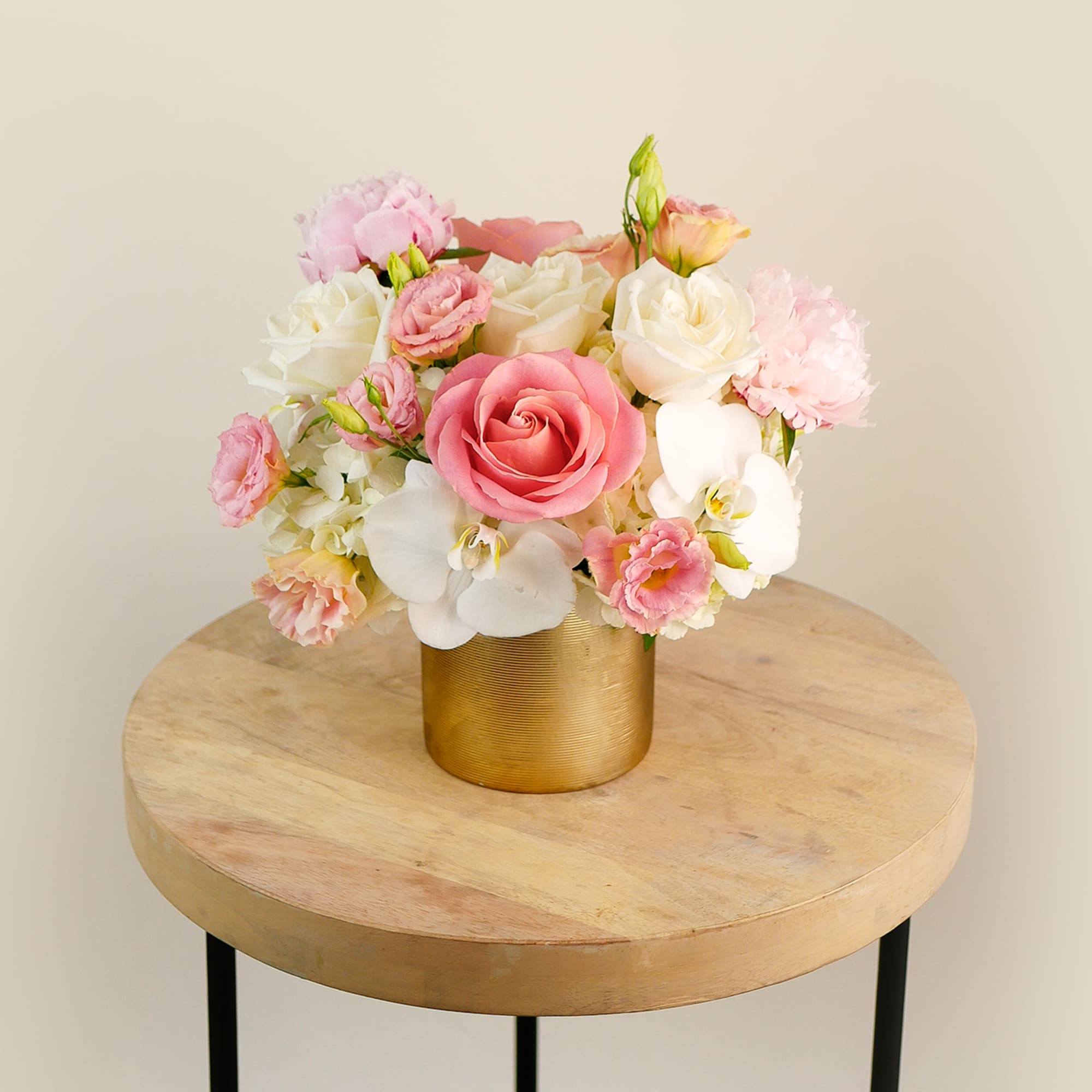 Pink and white flower arrangement in a gold vase on a round table