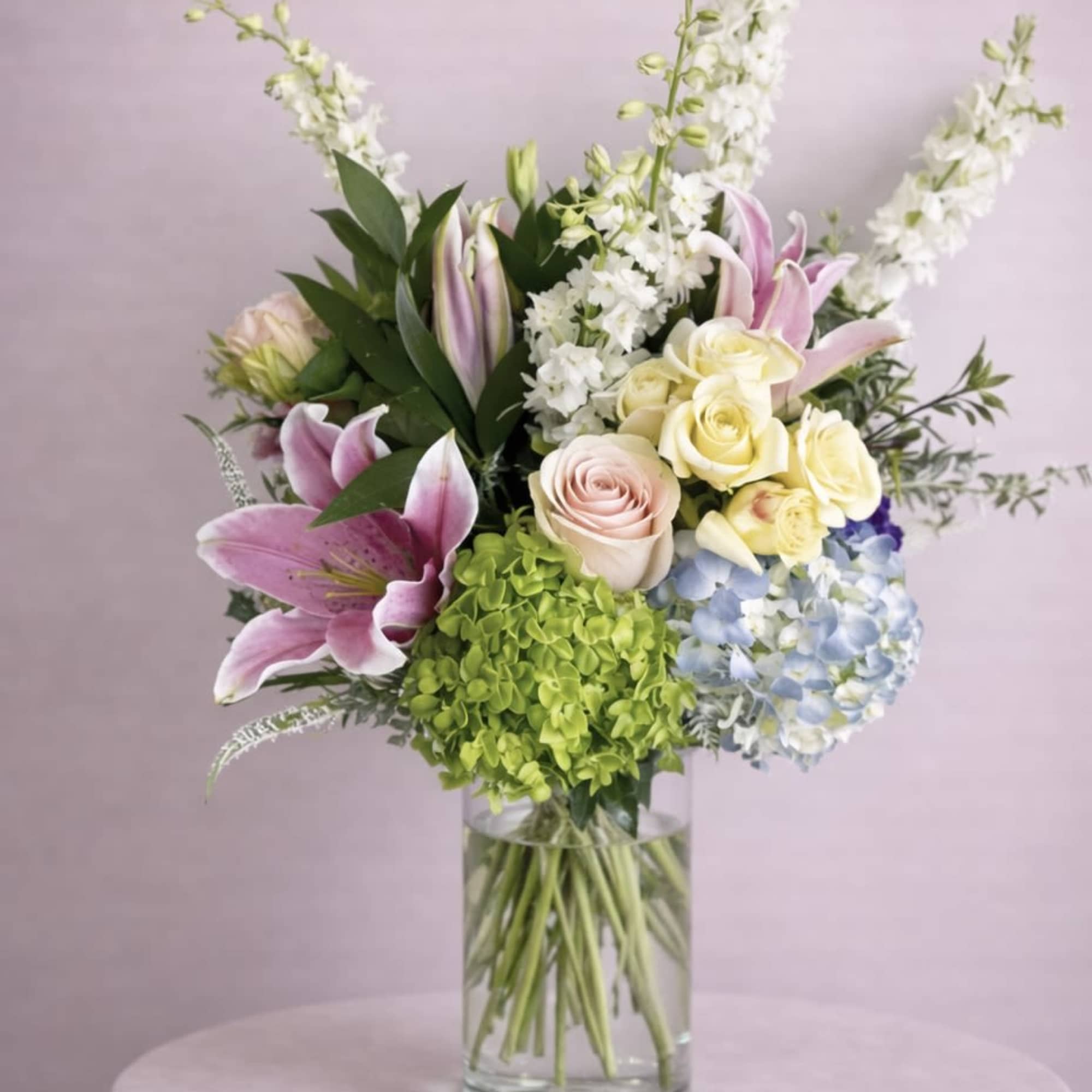 Mixed bouquet of lilies, roses, hydrangea, and white spikes in a glass vase