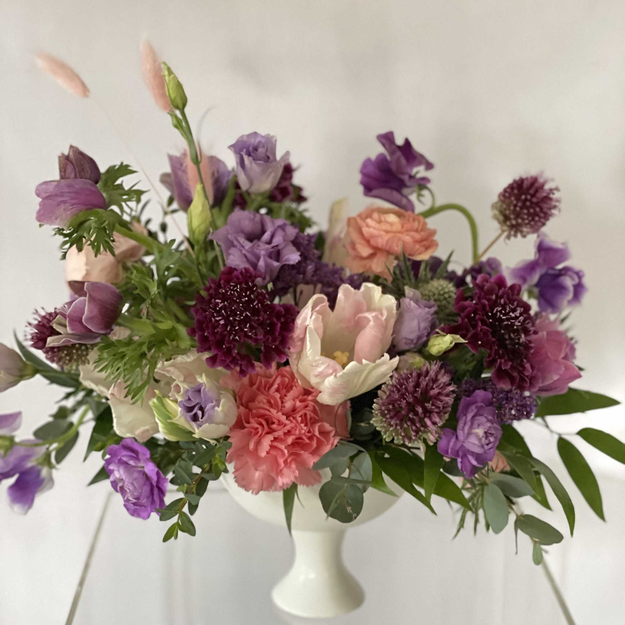Purple and pink mixed bouquet in a white pedestal vase
