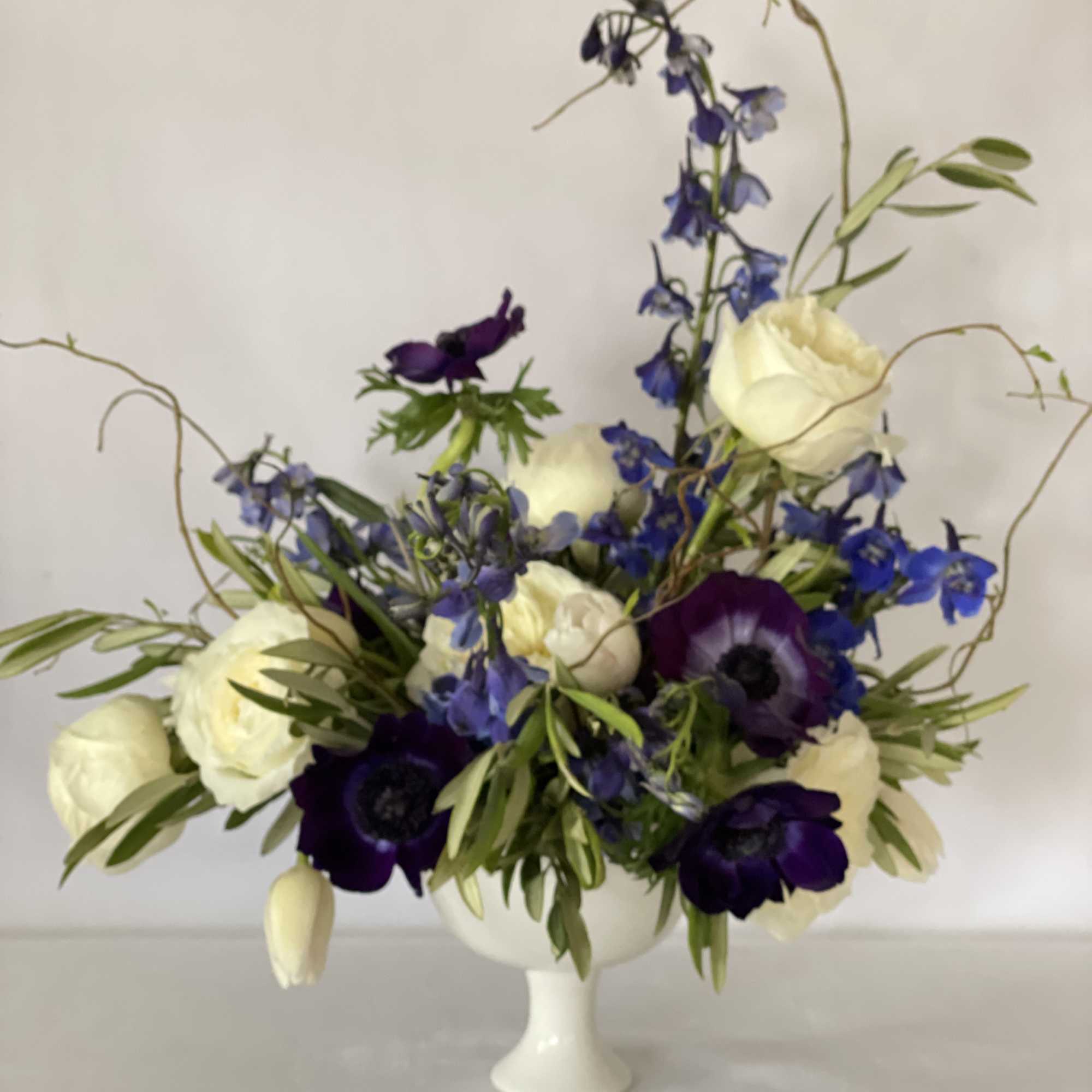 White and deep purple flowers arranged in a white pedestal vase