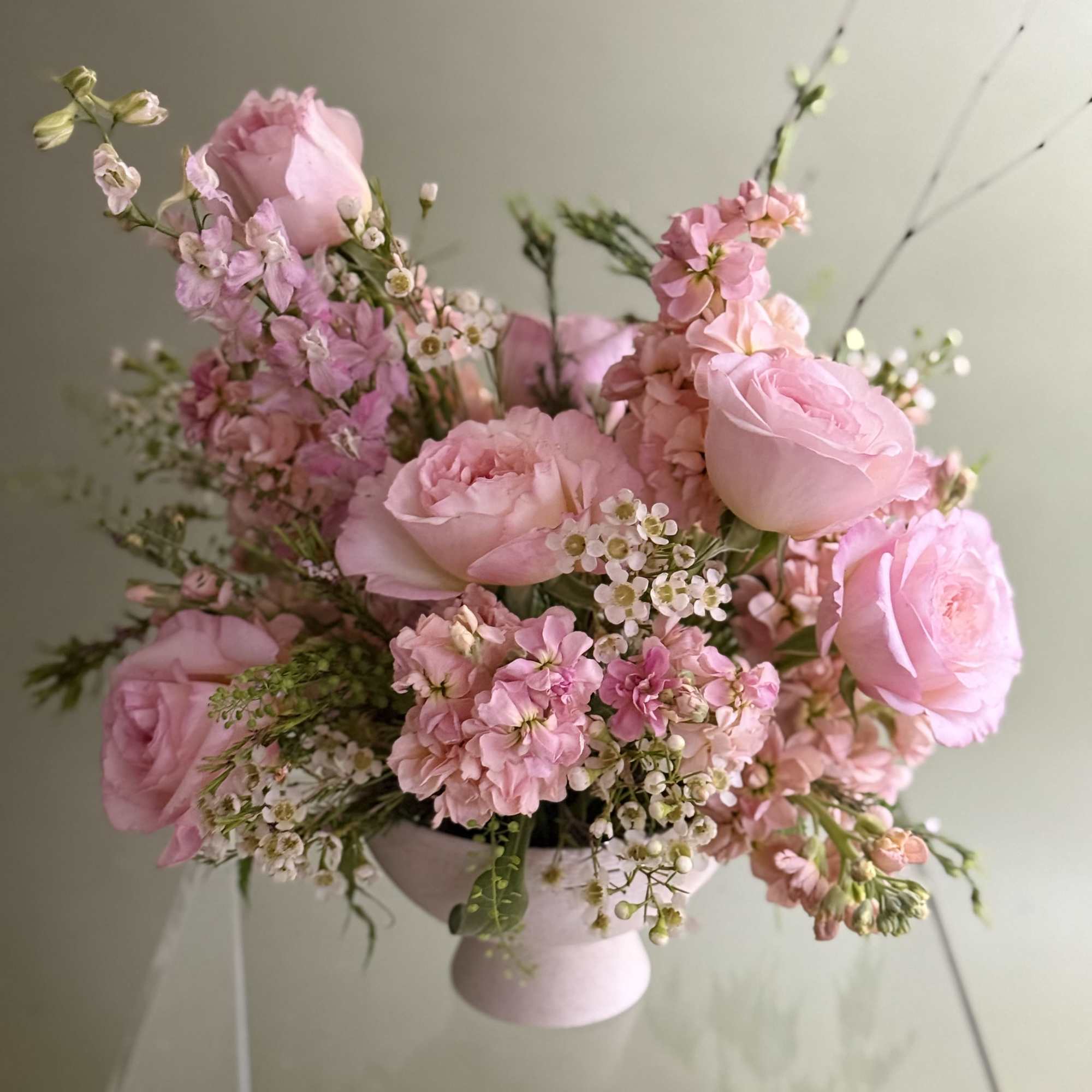 Pink roses and small blossoms arranged in a pale pedestal vase