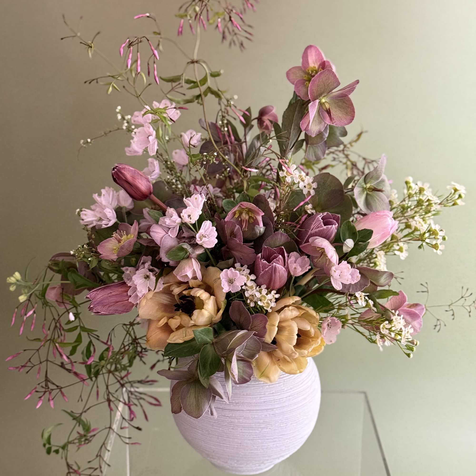 Loose pink and peach floral arrangement in a pale lavender vase
