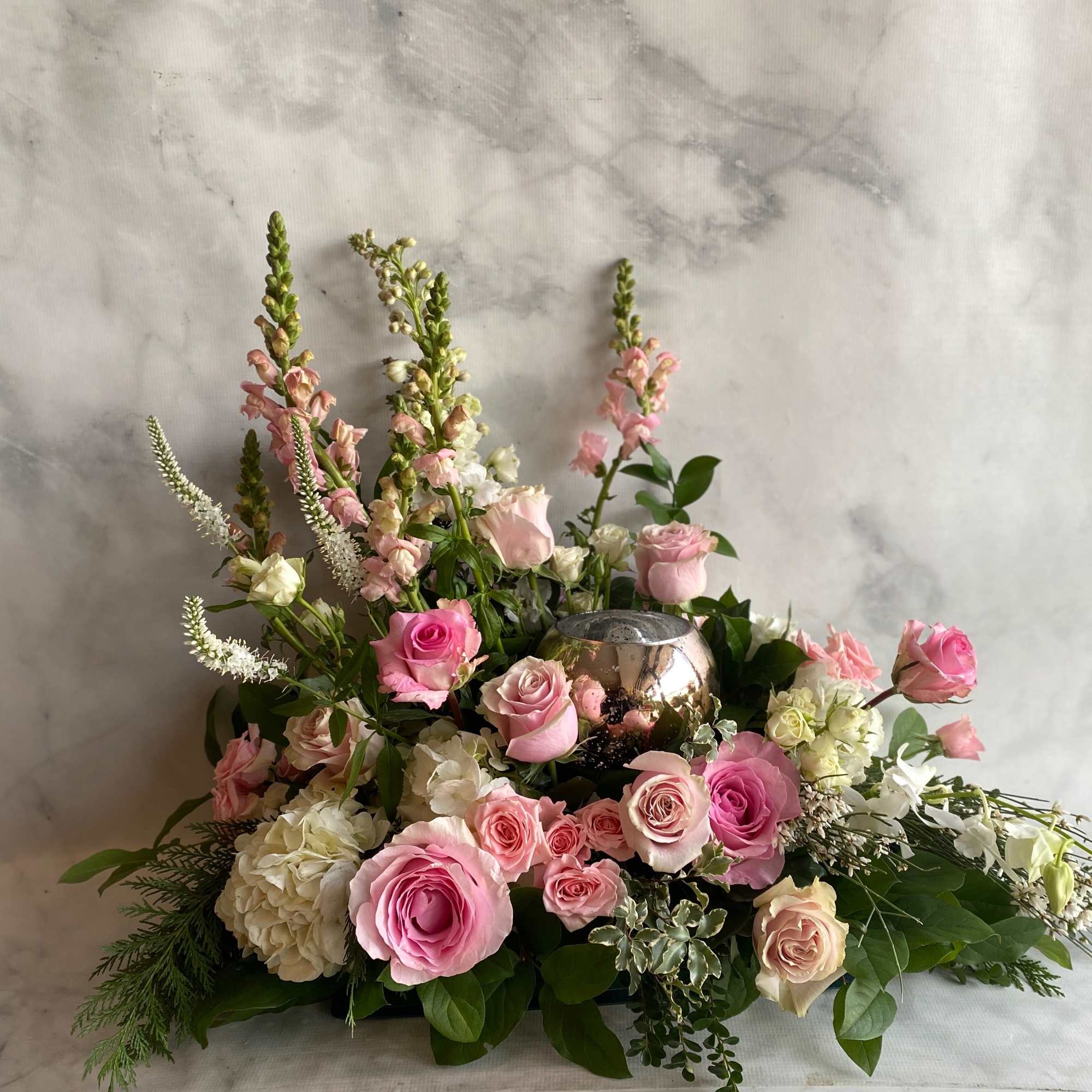 Pink and white roses with tall snapdragons in a low floral arrangement