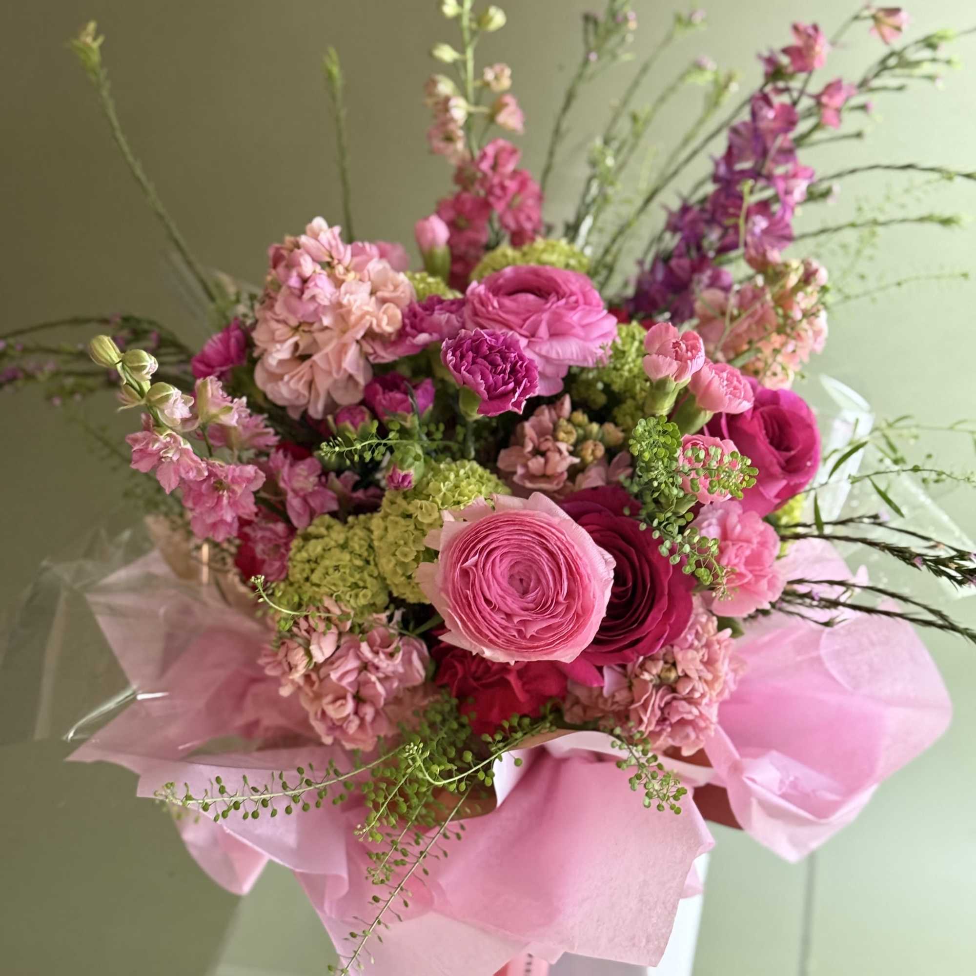 Pink mixed bouquet with ranunculus, carnations, and tall accent blooms in pink wrap