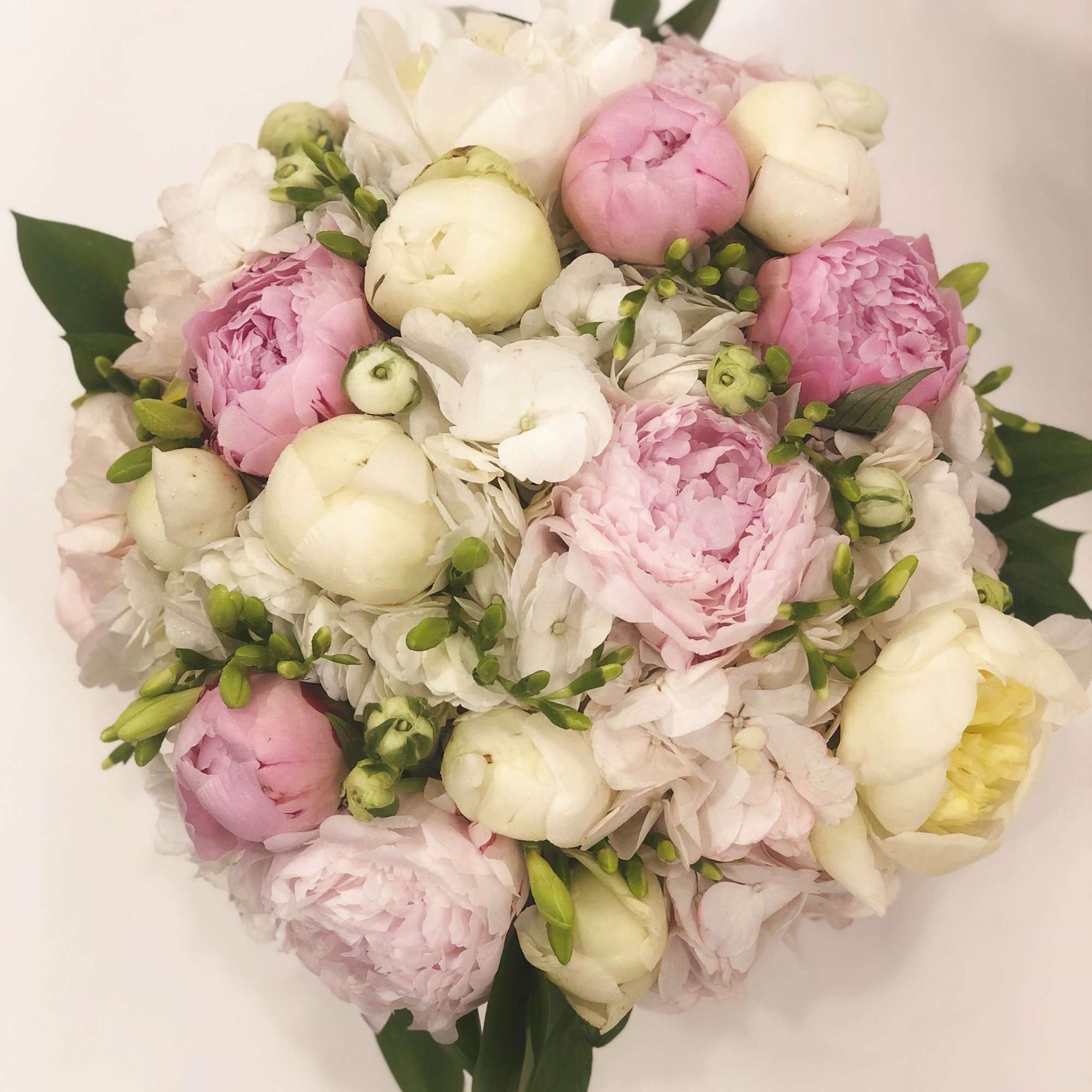 Round bouquet of pink and white peonies with green accents