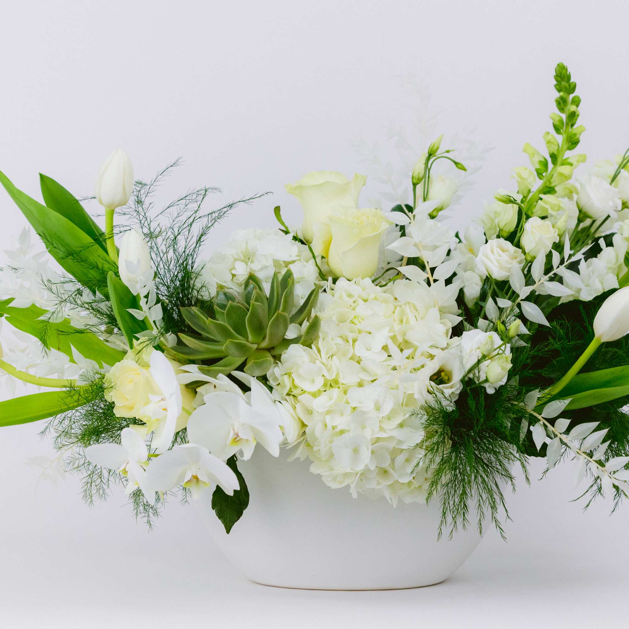 White floral arrangement in a white bowl vase with green accents