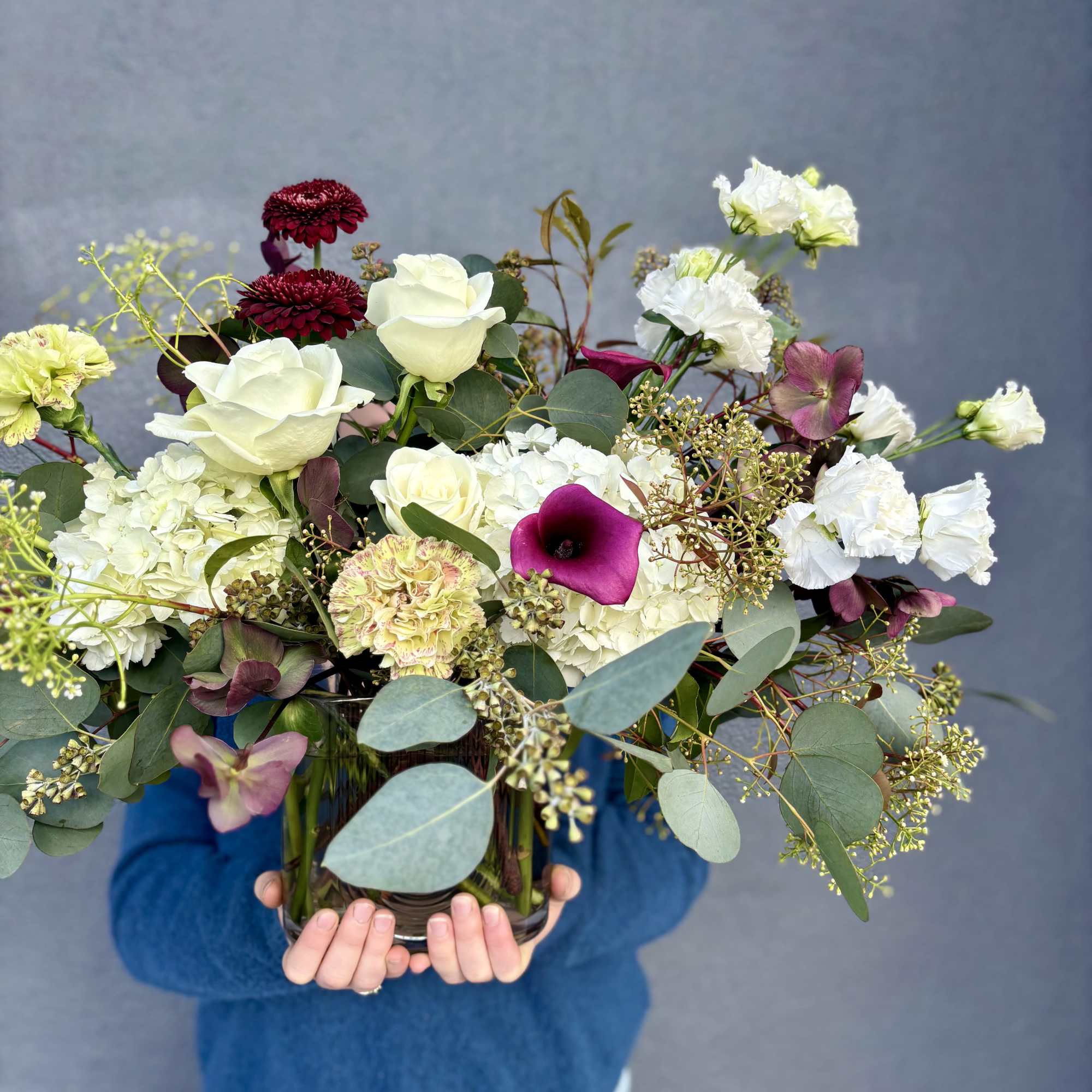 Mixed bouquet with white roses, burgundy blooms, and a purple calla lily in a glass vase.