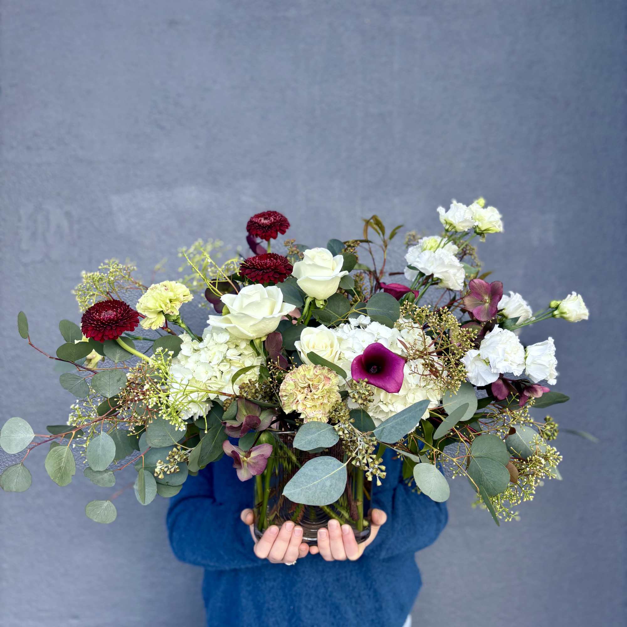 Large mixed bouquet in a glass vase with white, burgundy, and purple blooms