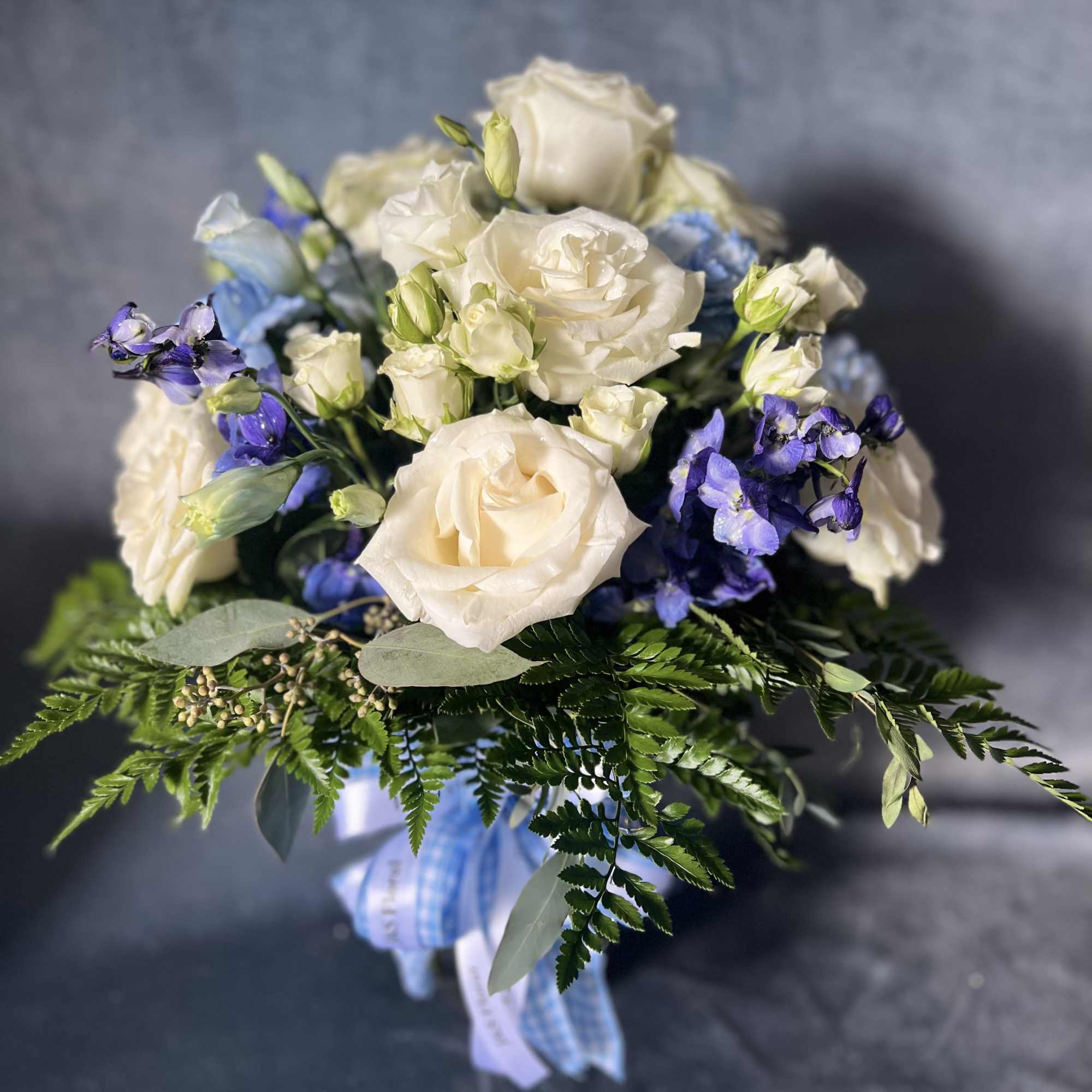 White roses and blue flowers in a hand-tied bouquet with ribbon