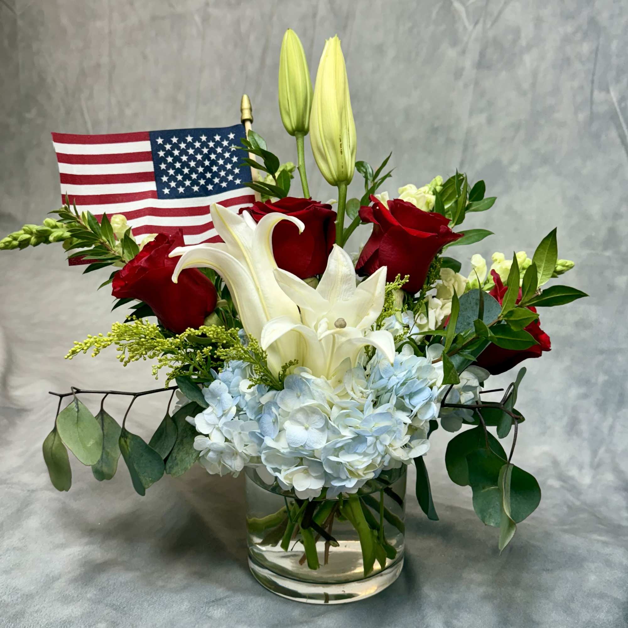 Red roses and white lilies in a glass vase with a small American flag