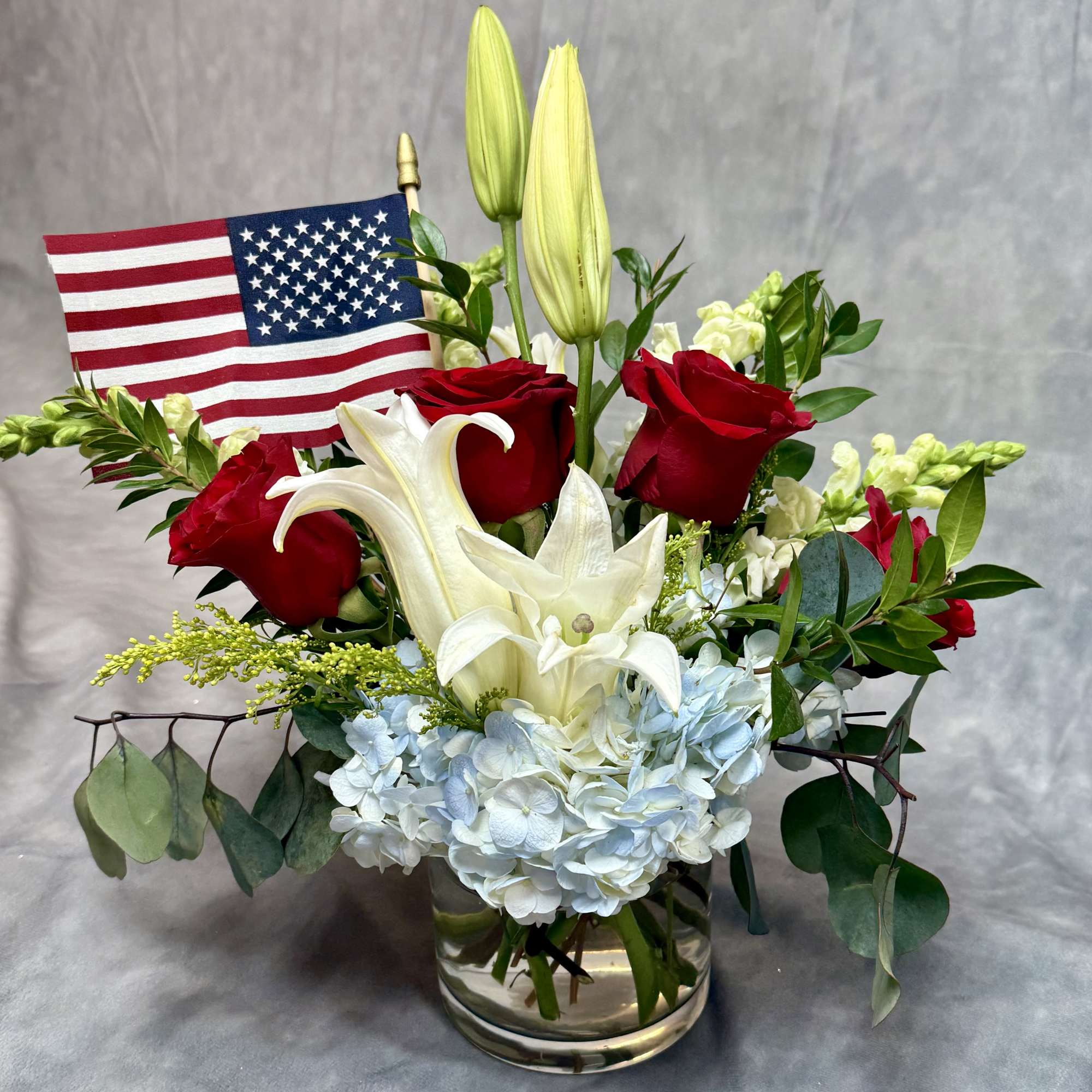 Red roses and white lilies in a glass vase with an American flag
