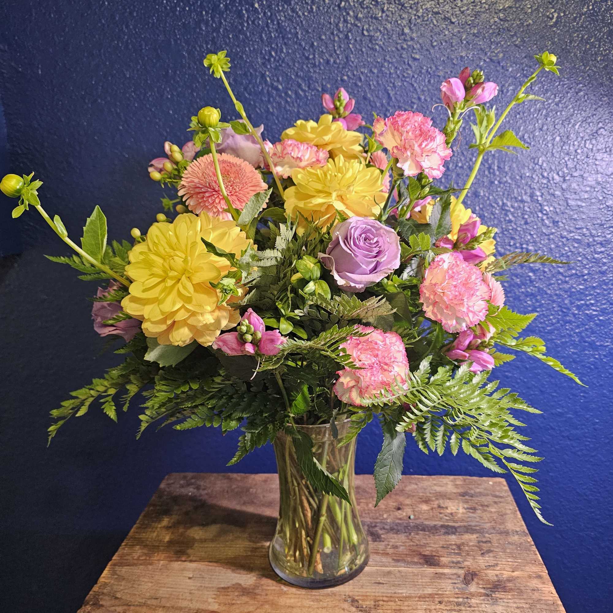 Mixed pink and yellow flowers arranged in a clear glass vase