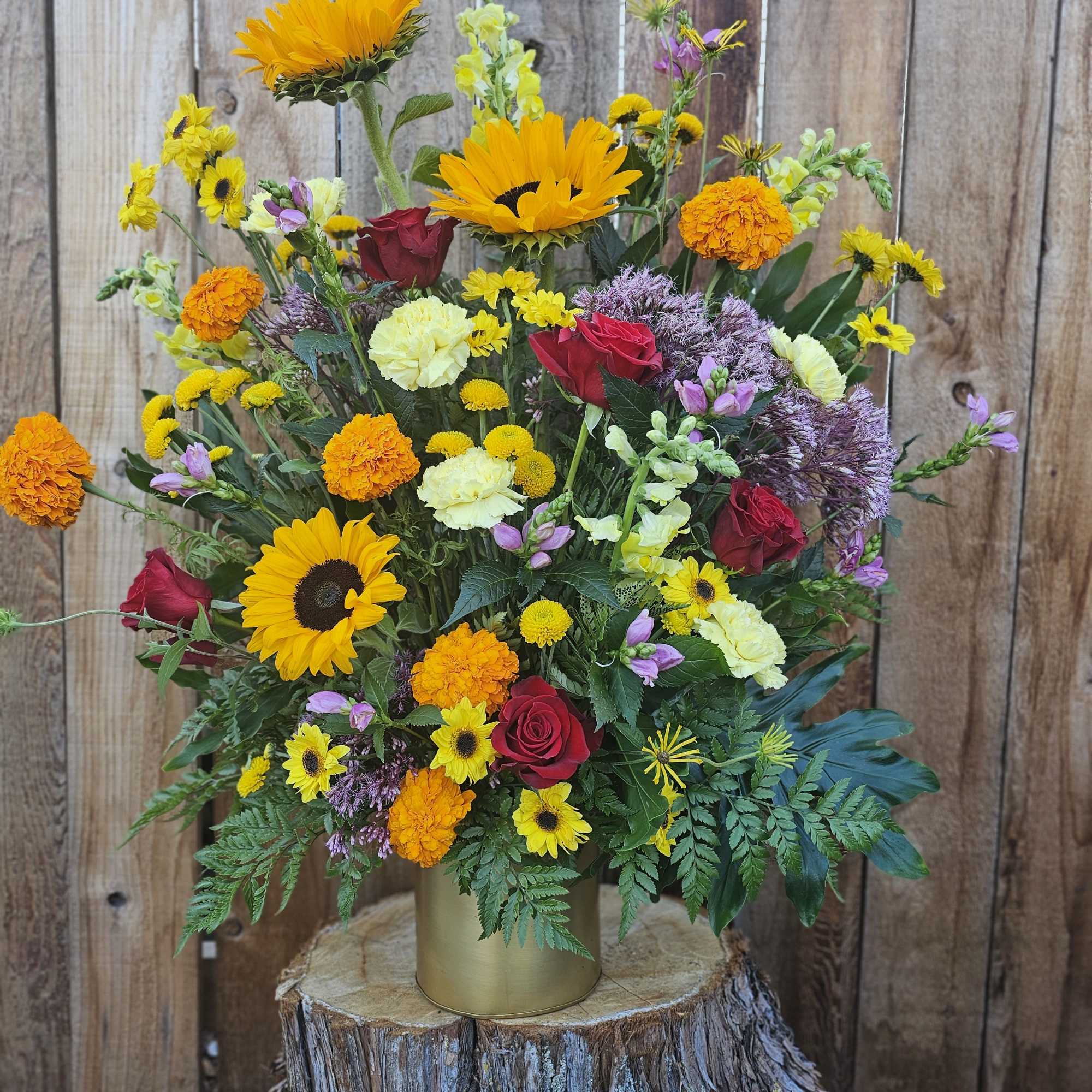 Mixed bouquet of sunflowers, roses, and marigolds in a gold vase