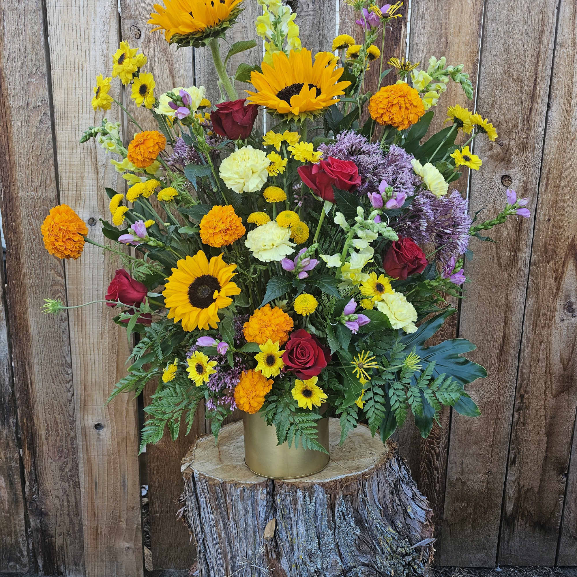Mixed bouquet with sunflowers, red roses, and orange marigolds in a gold vase