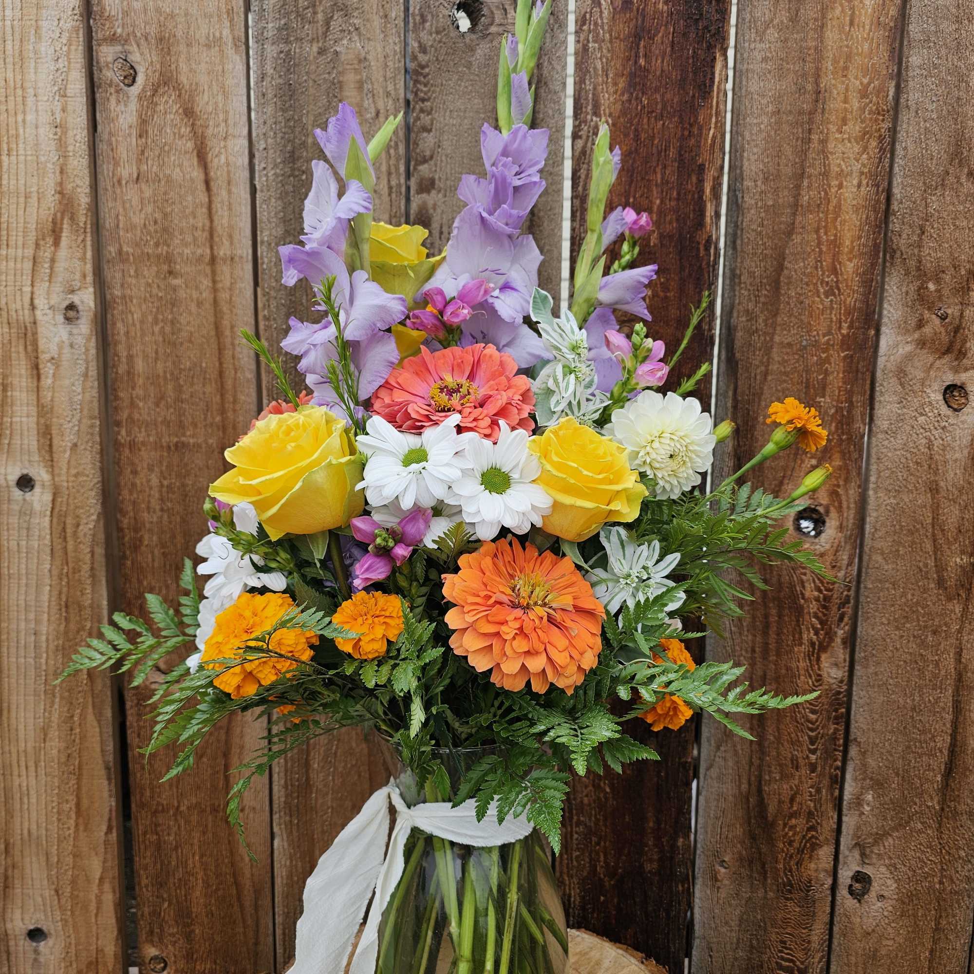Tall mixed bouquet with yellow roses, orange and white blooms, and lavender spikes in a clear vase with white ribbon