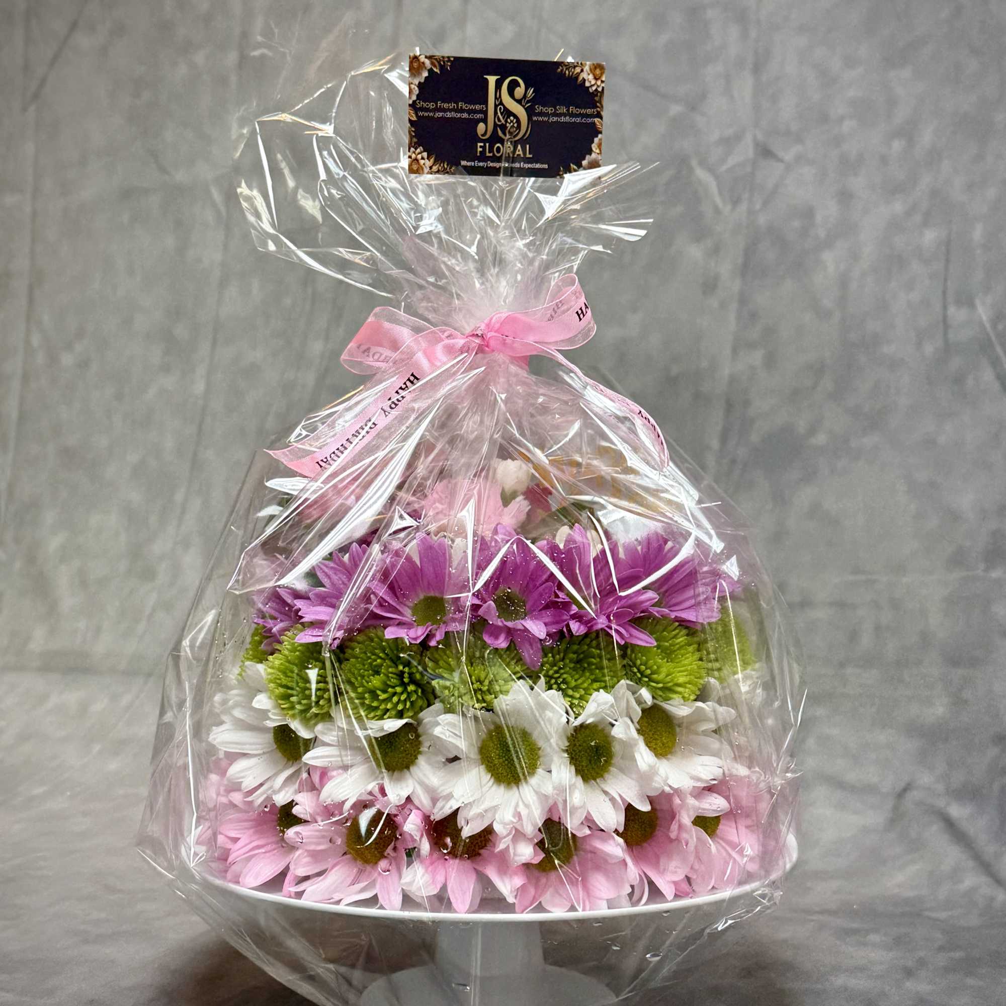 Wrapped bouquet of pink, white, and green daisies in a white container