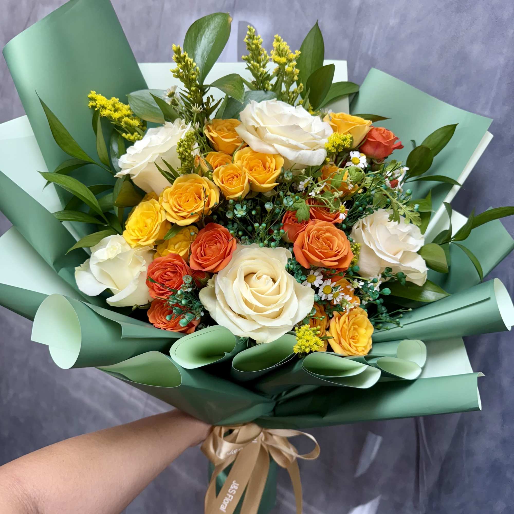 Bouquet of white, yellow, and orange roses wrapped in green paper