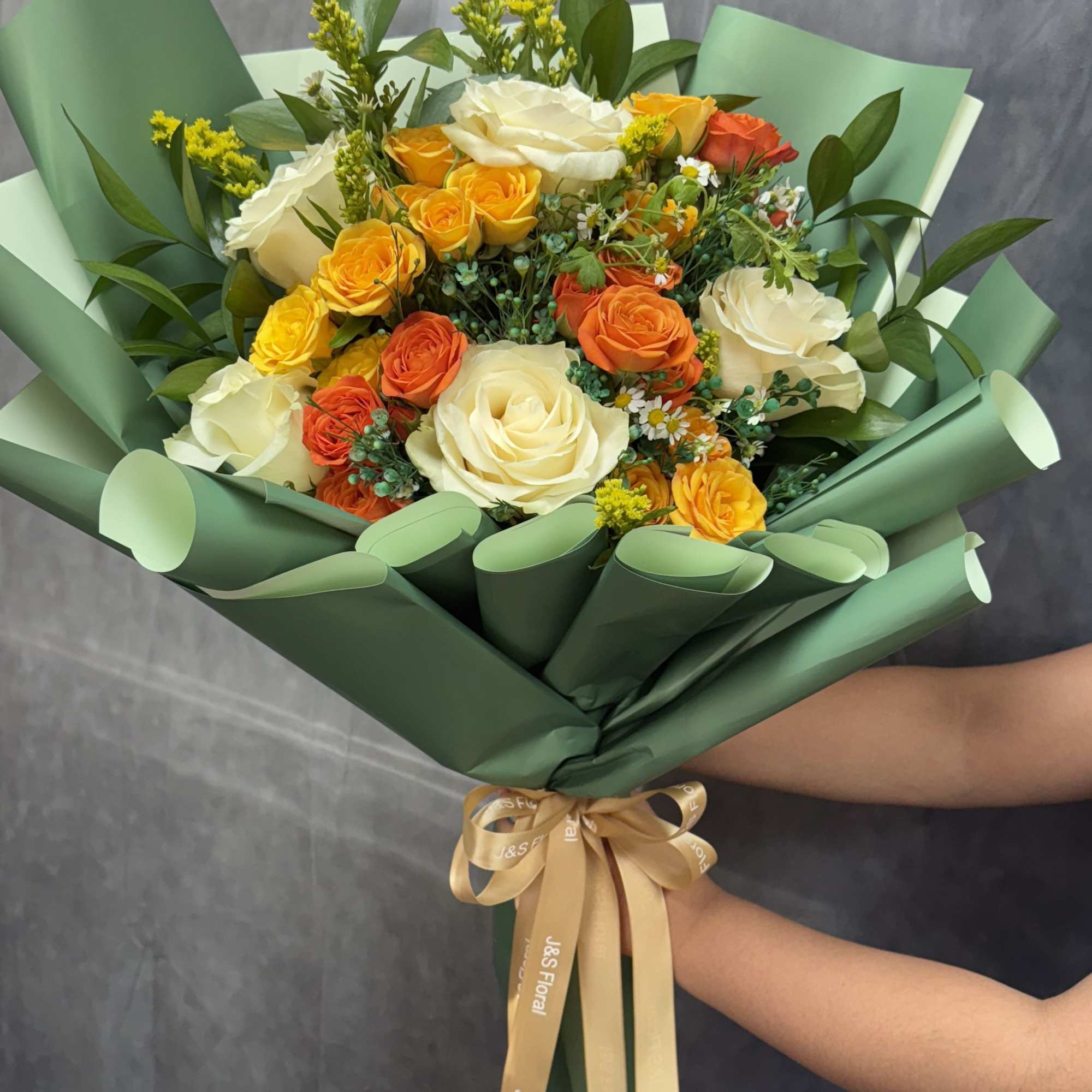 Bouquet of cream, yellow, and orange roses wrapped in green paper