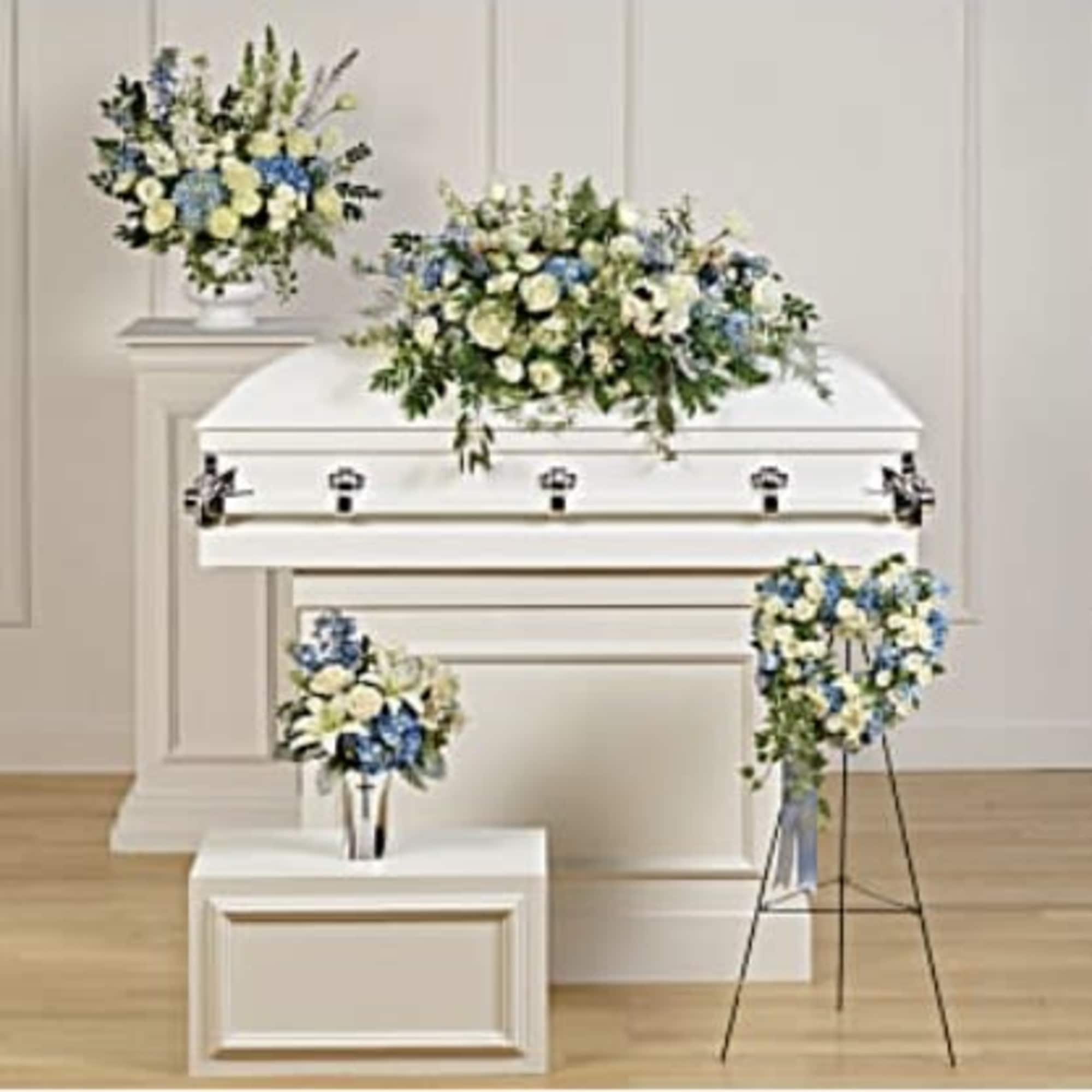 White casket with blue and white floral sprays in a funeral room