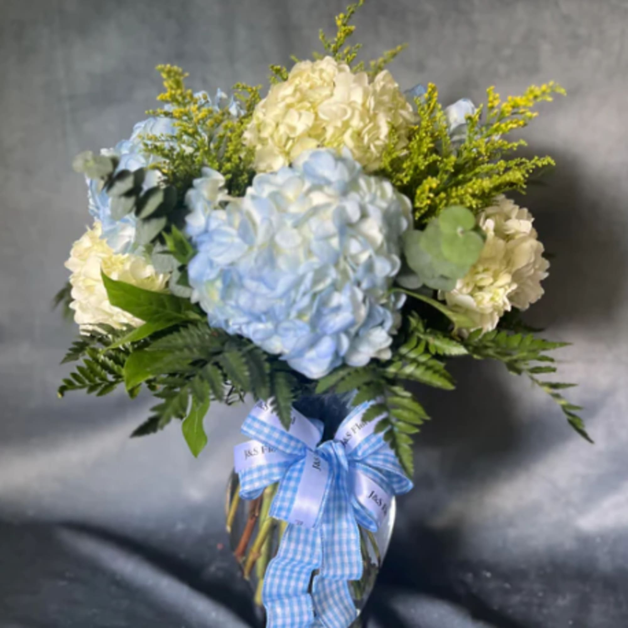 Blue and white hydrangea bouquet in a glass vase with a blue ribbon