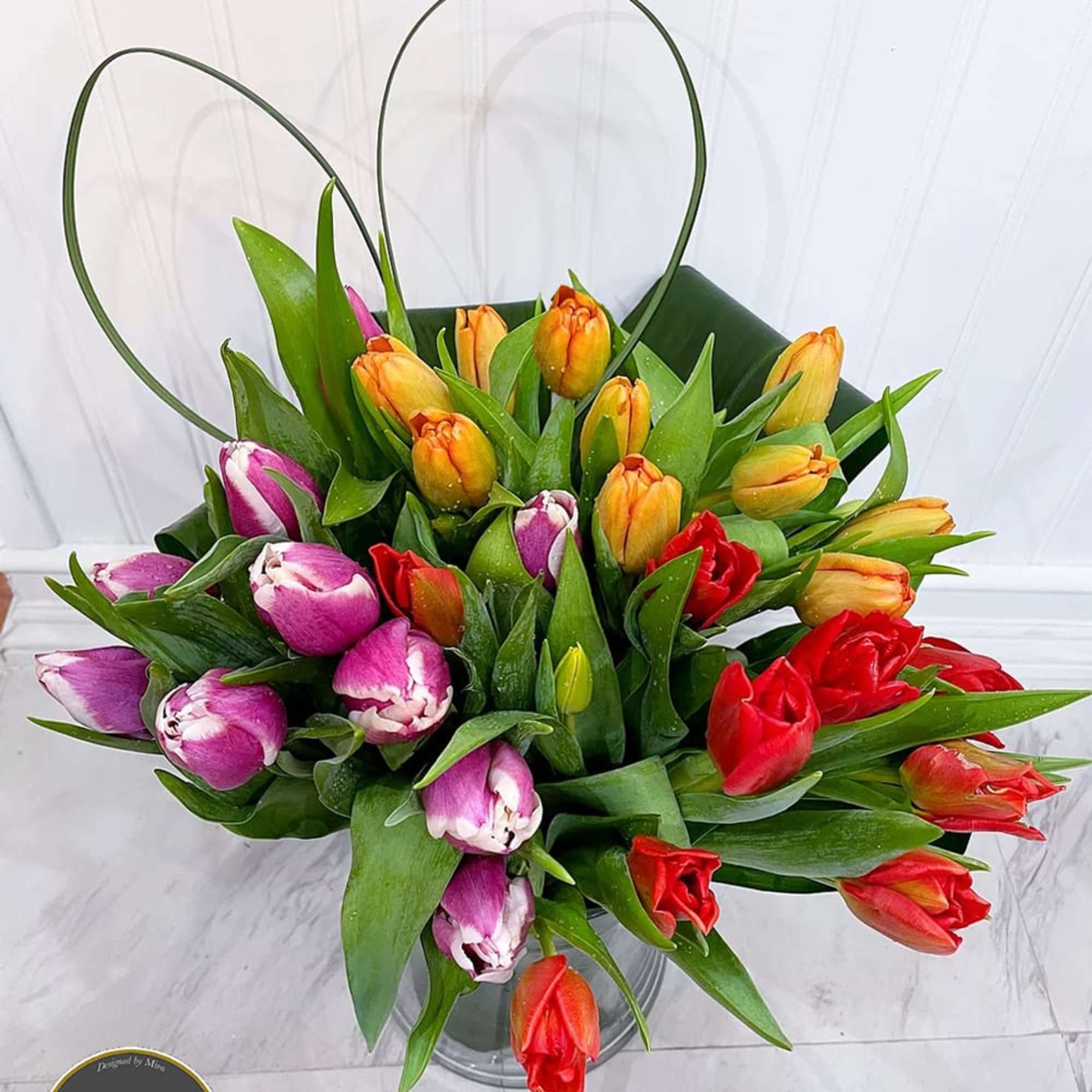 Multicolored tulip arrangement with orange, red, and purple blooms in a clear glass vase