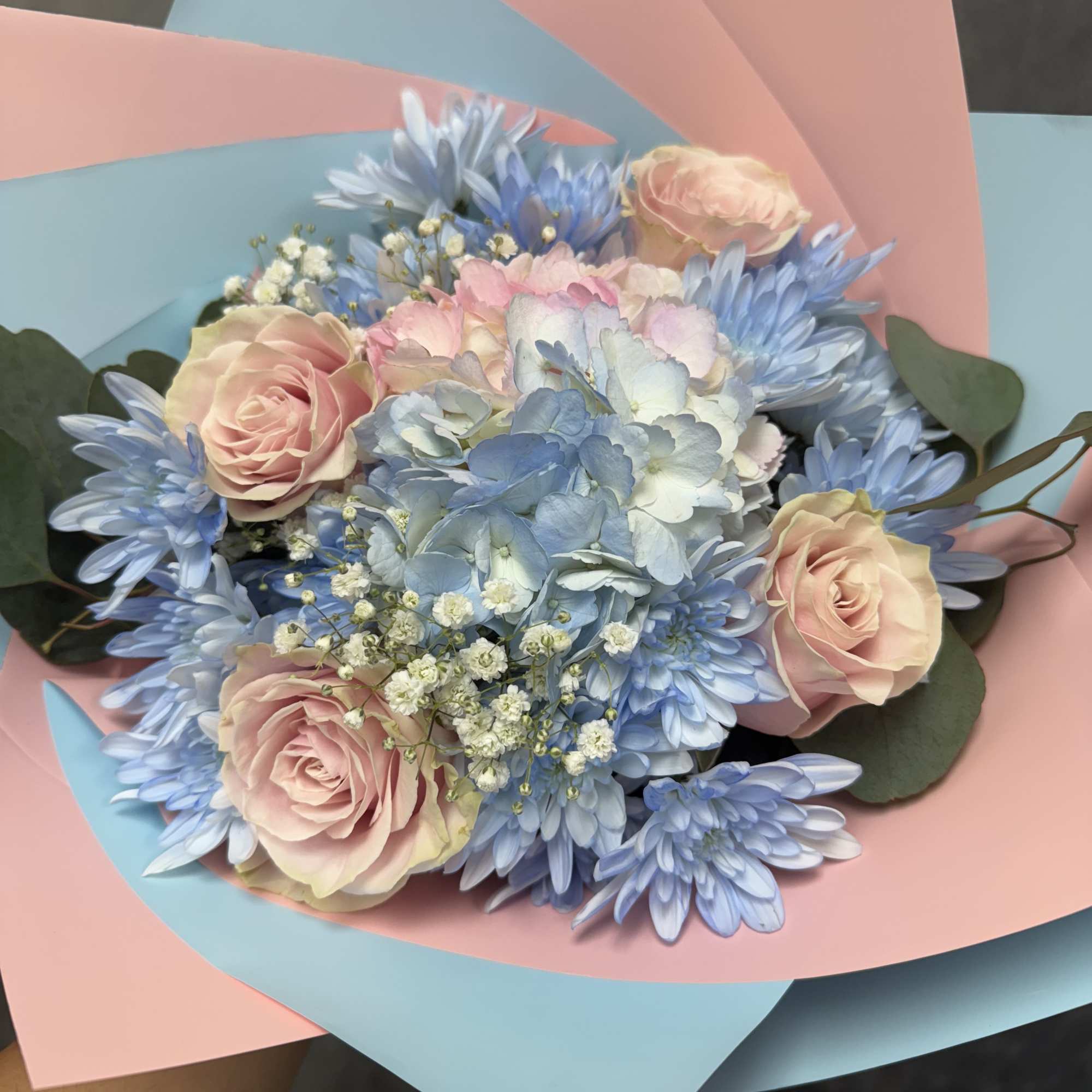 Bouquet of pale pink roses and blue flowers wrapped in pink and blue paper