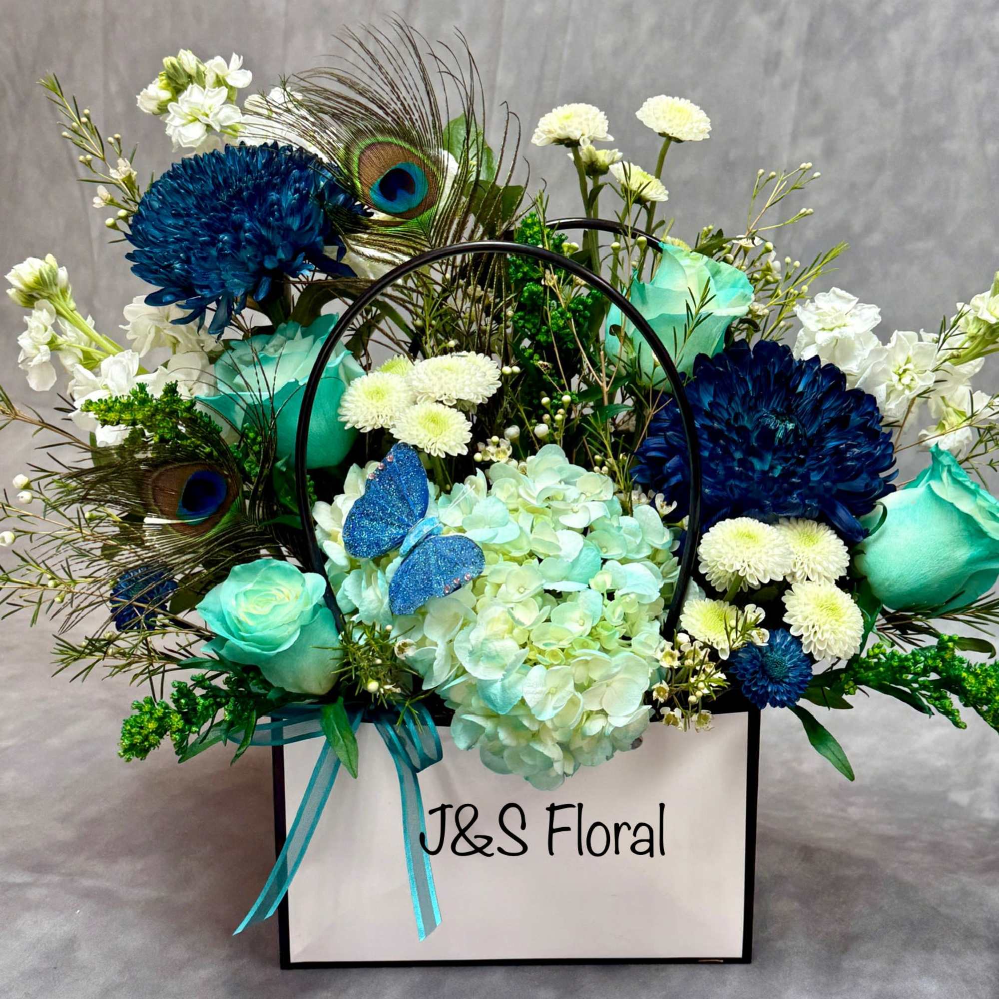 Blue and white floral arrangement in a white gift box with peacock feathers