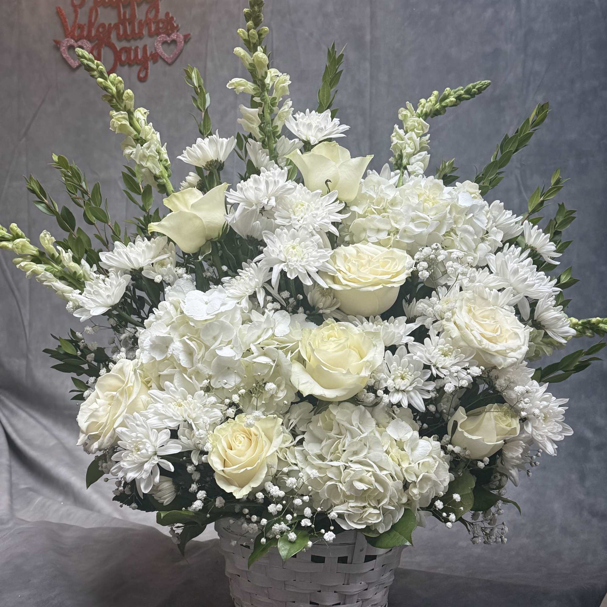White floral arrangement in a woven basket with roses, hydrangeas, and daisies
