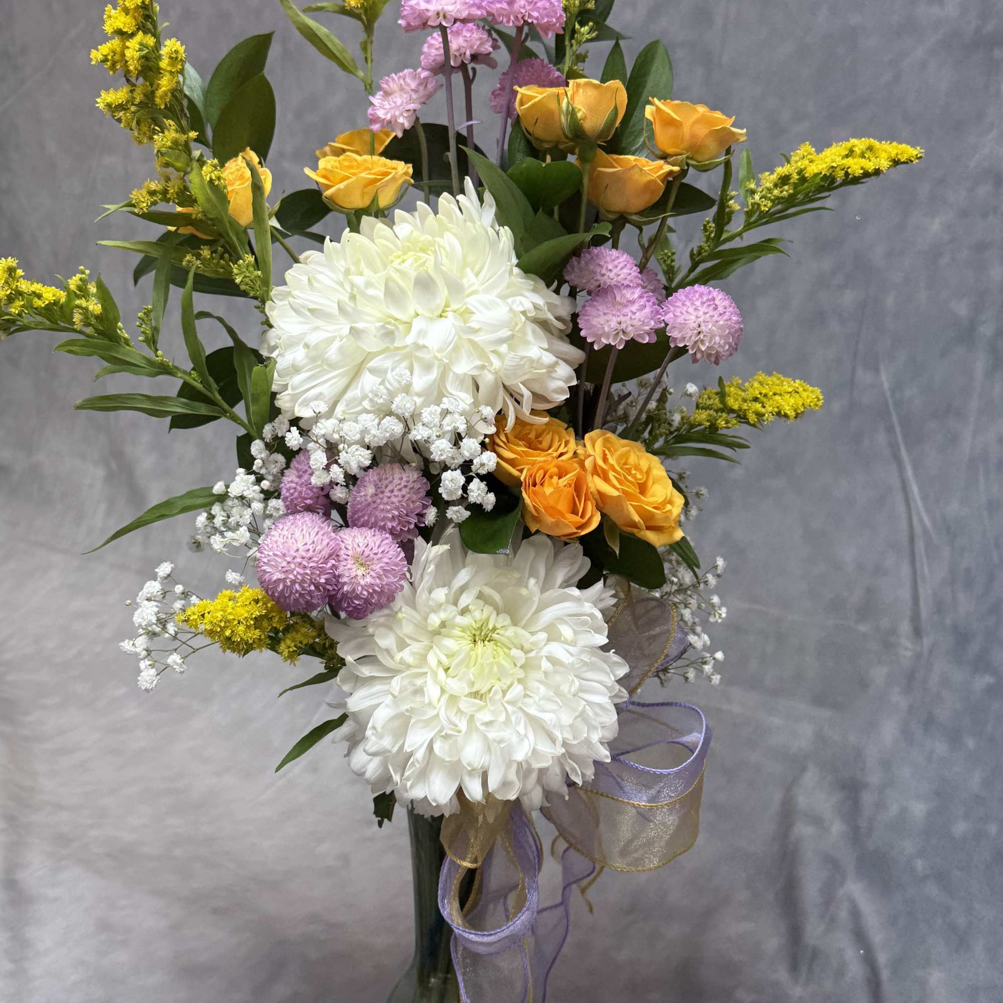 Tall bouquet of white chrysanthemums, yellow roses, and lavender flowers in a glass vase
