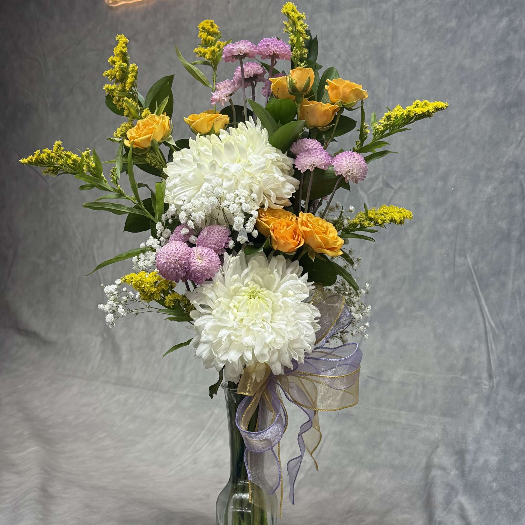 Mixed bouquet of white chrysanthemums, yellow roses, and pink pompons in a glass vase