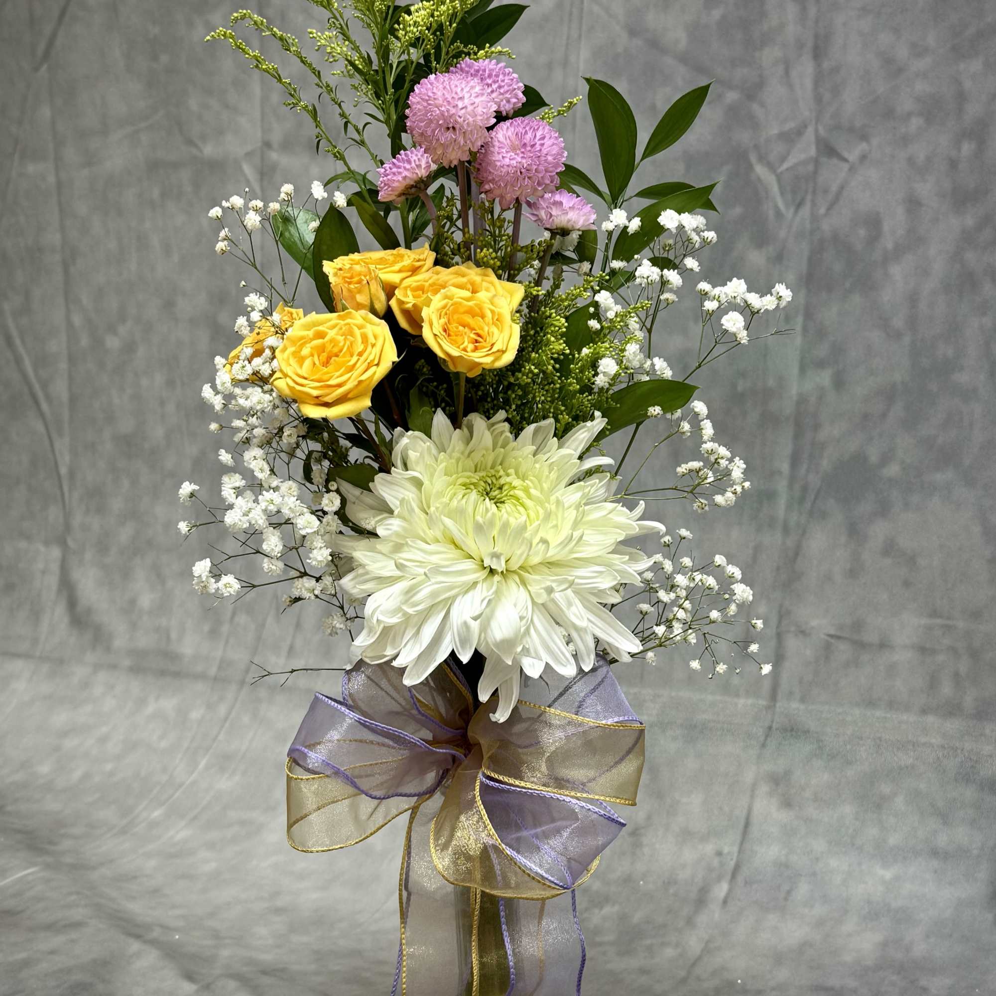 Tall bouquet of yellow and white flowers in a glass vase with a ribbon bow