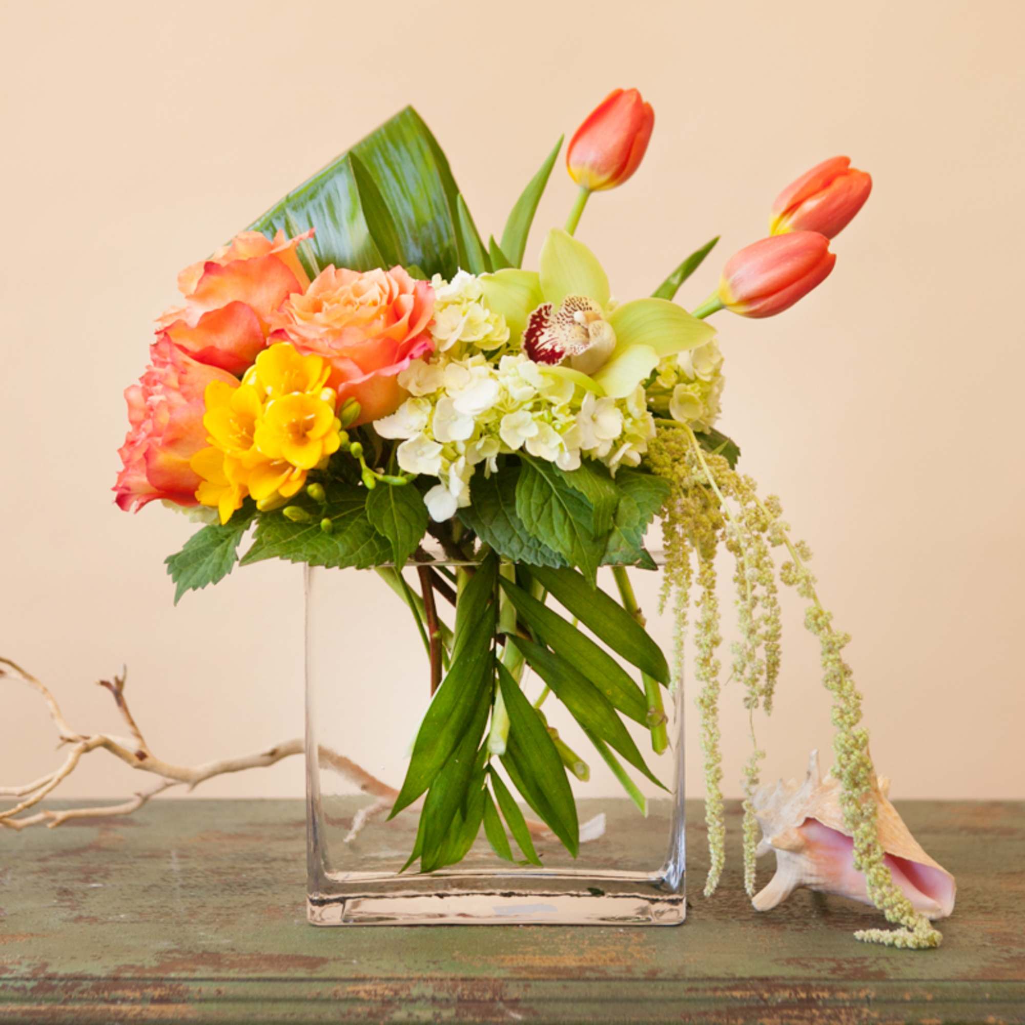 Mixed bouquet in a clear glass vase with tulips, roses, and orchids