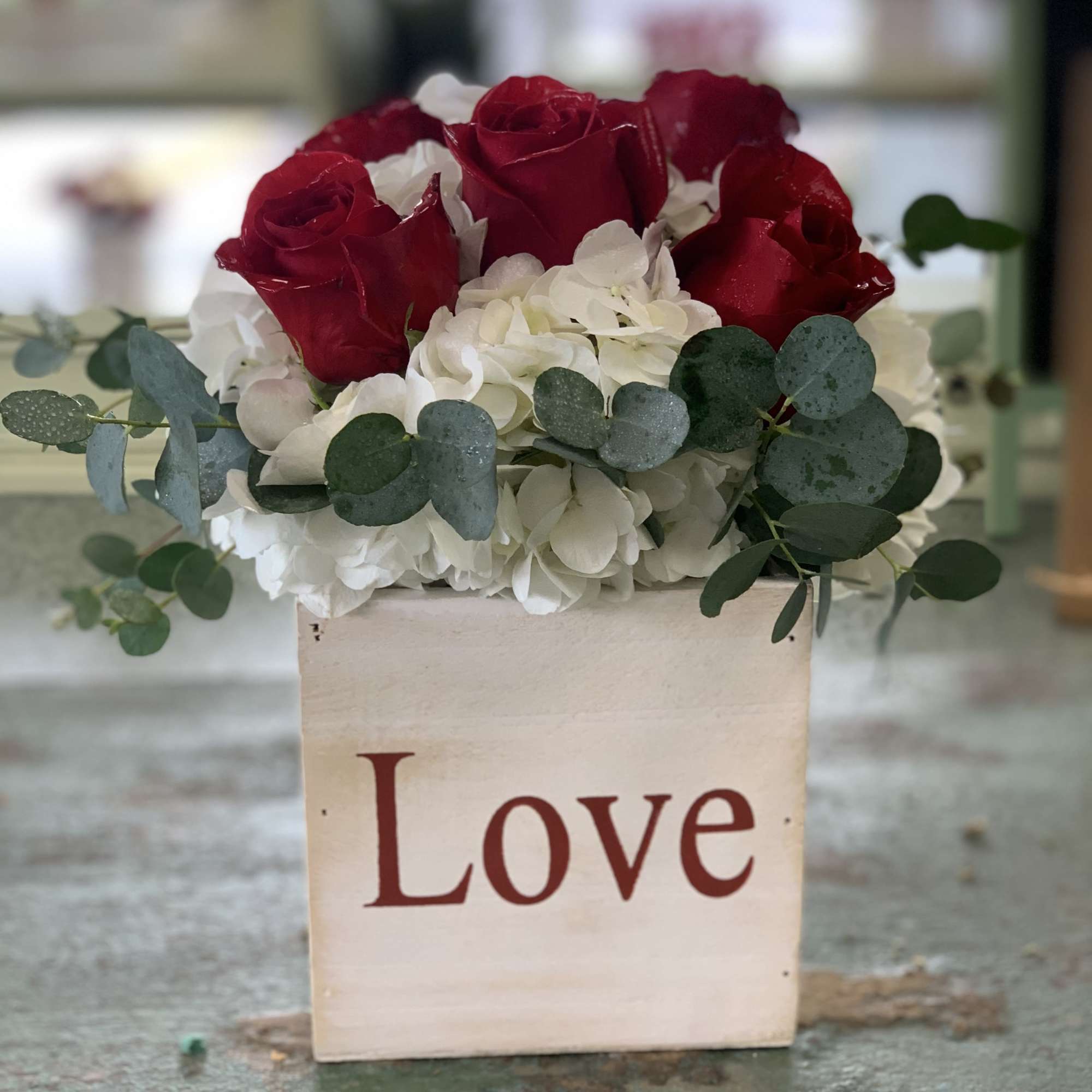 Red roses and white hydrangeas in a wooden box labeled Love